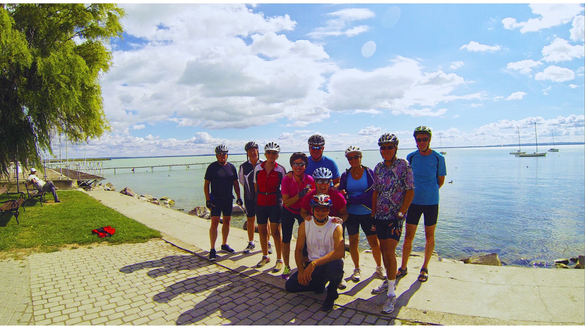 A group of people standing on a path beside a body of water, enjoying the view and each other's company.