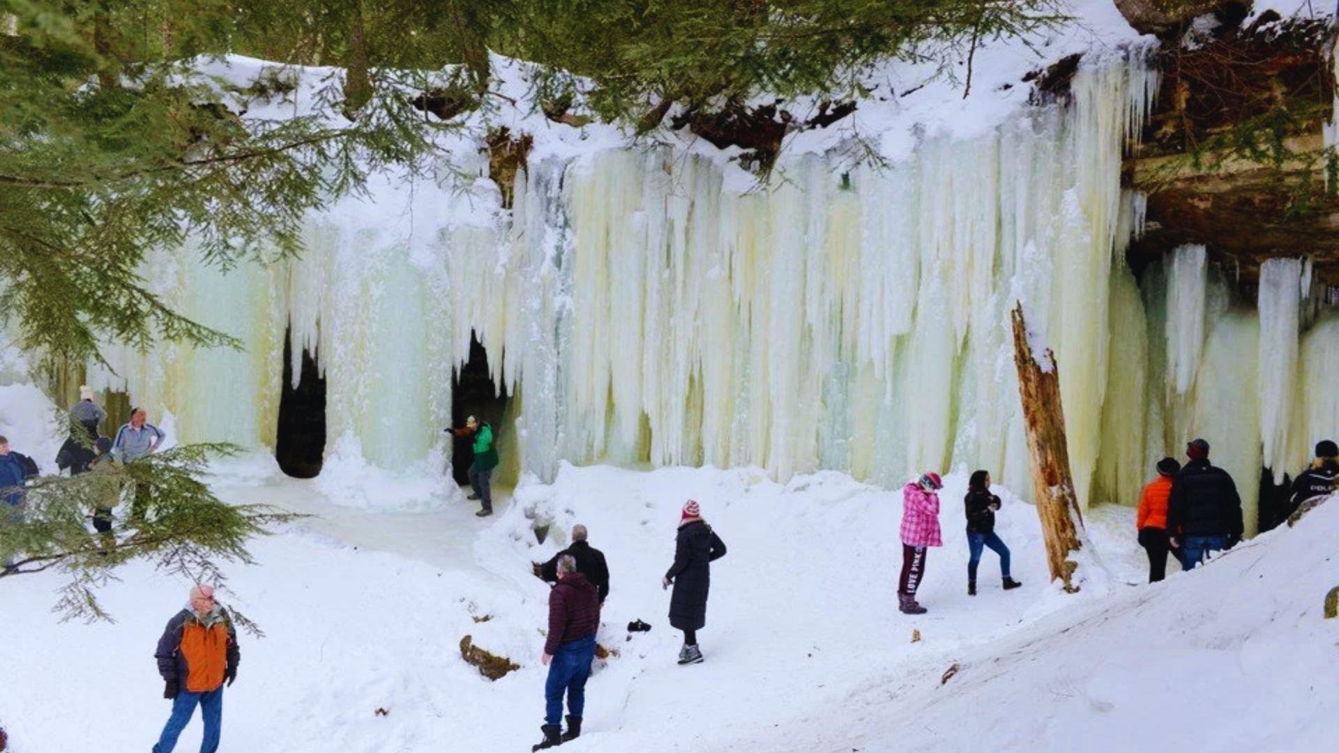 People gather around a snowy waterfall, enjoying the winter scenery and the sound of cascading water.