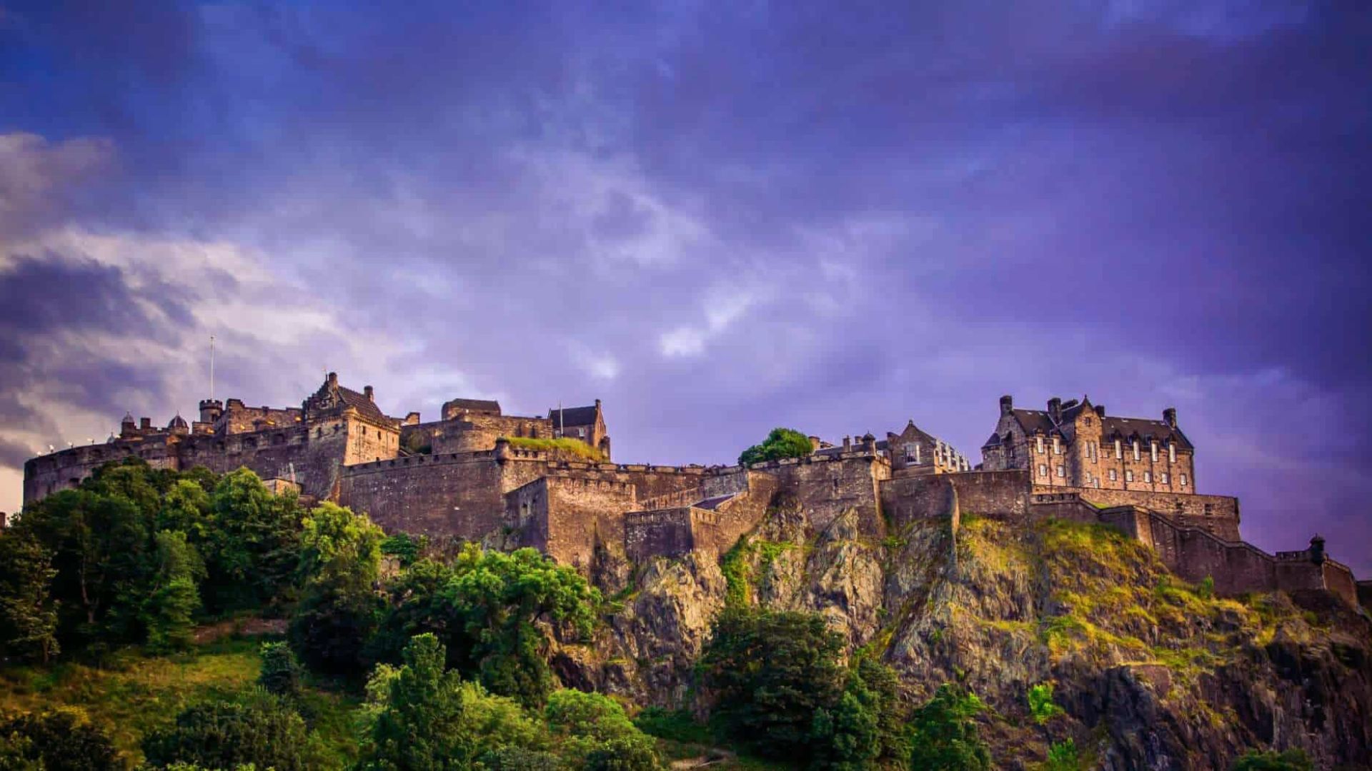 . Edinburgh Castle stands majestically under a cloudy sky, showcasing its historic architecture against a dramatic backdrop.