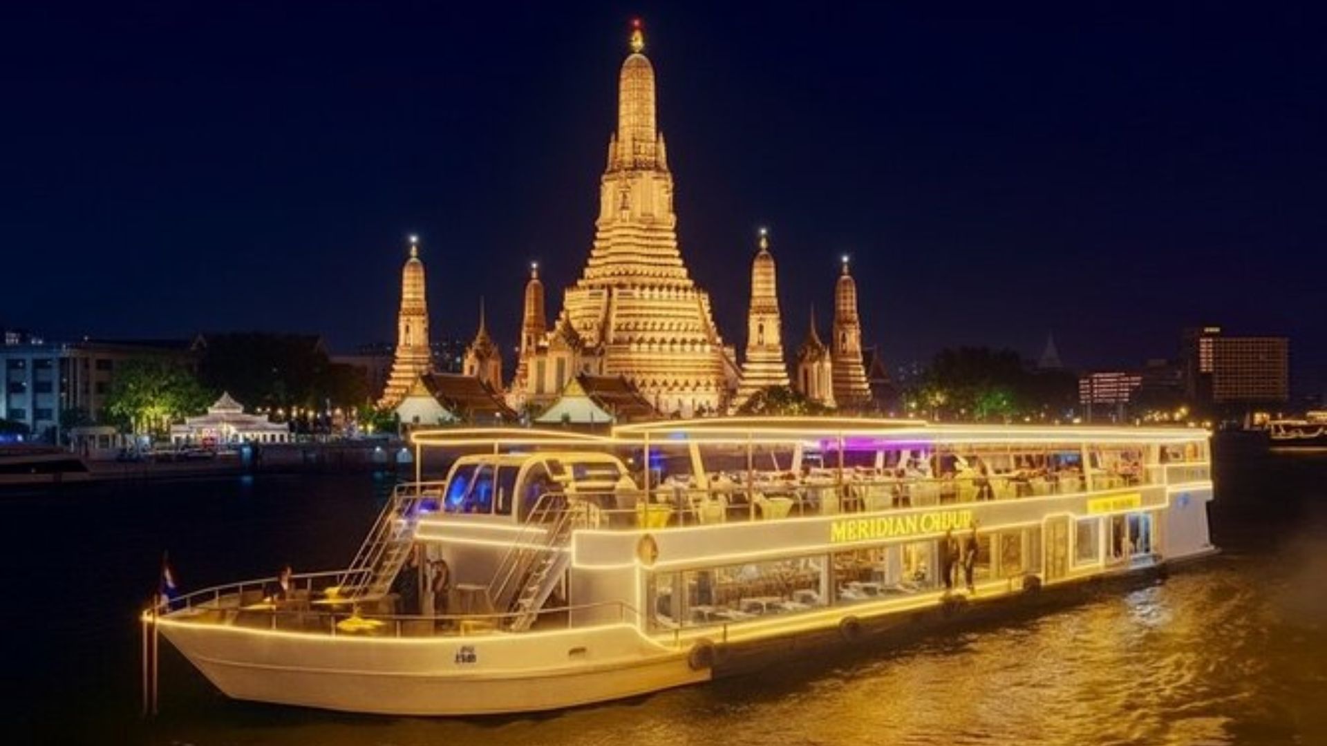 A boat floats on the river with a large building visible in the background against a clear sky.
