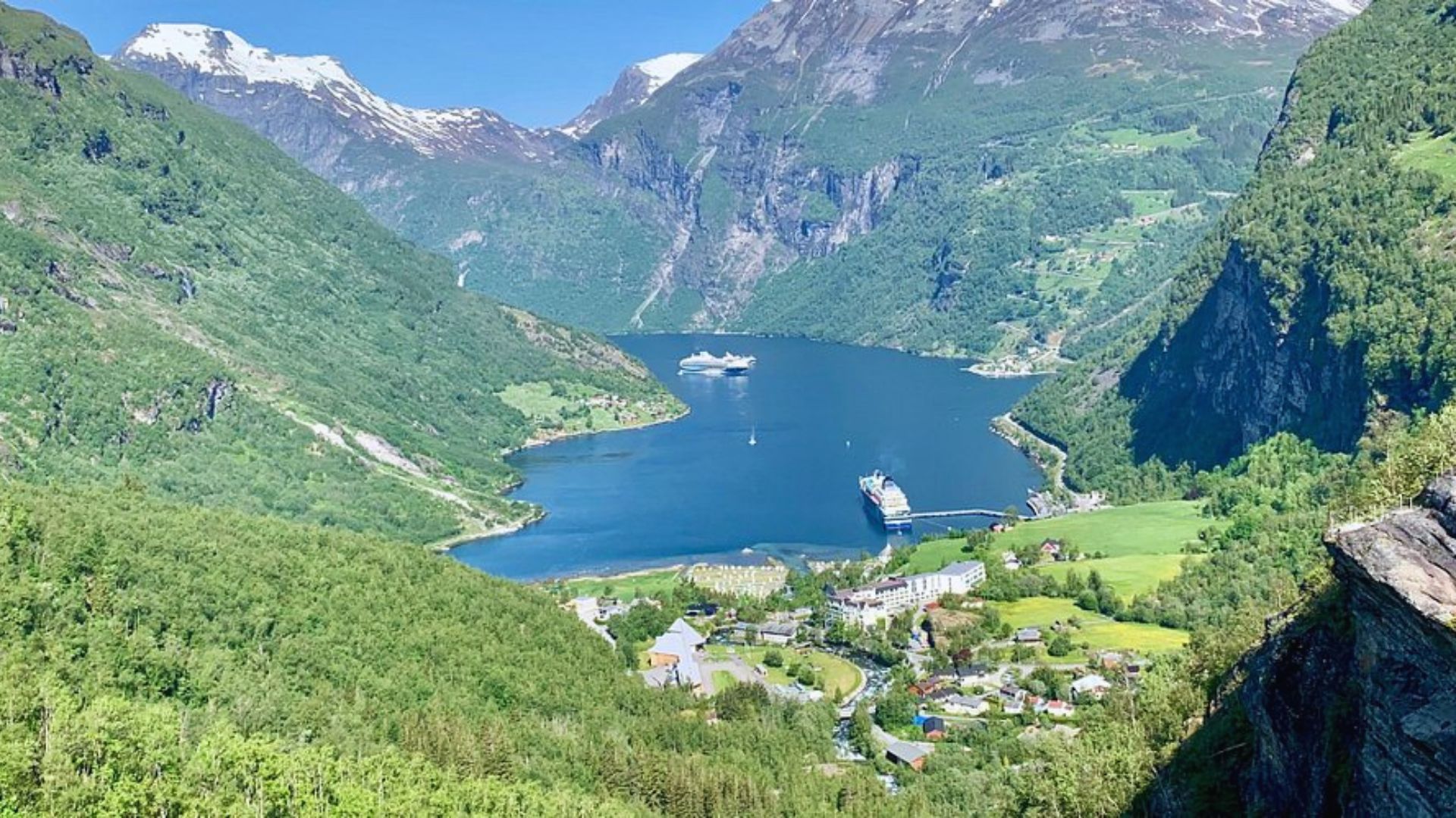 . A panoramic view from a mountain peak, showcasing a stunning fjord surrounded by steep cliffs and lush greenery.