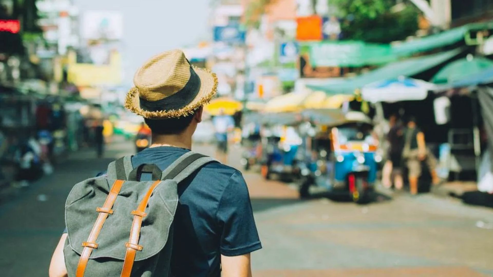 A man carrying a backpack walks along a city street, surrounded by buildings and trees.