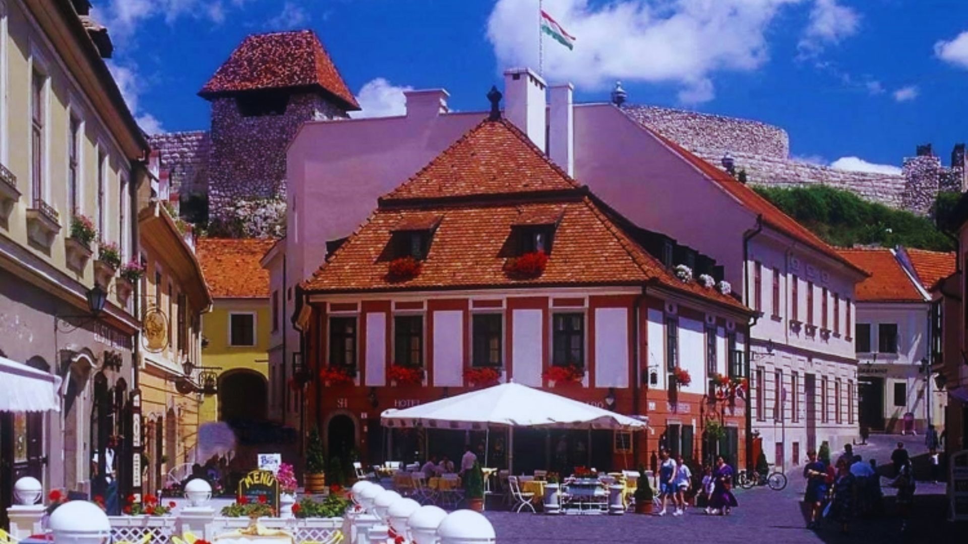 A street lined with buildings, featuring a castle prominently in the background against a clear sky.
