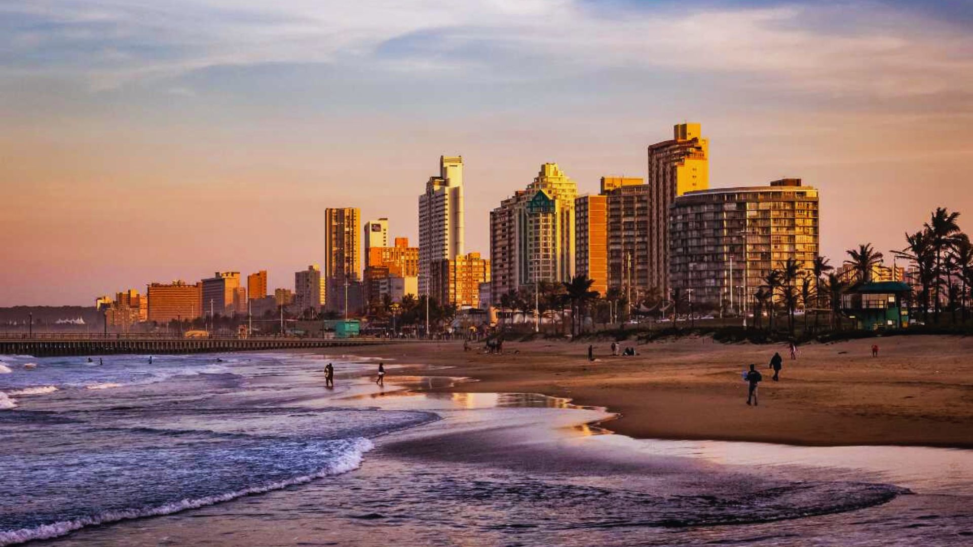 A beach scene featuring golden sand with tall buildings rising in the background against a clear blue sky.