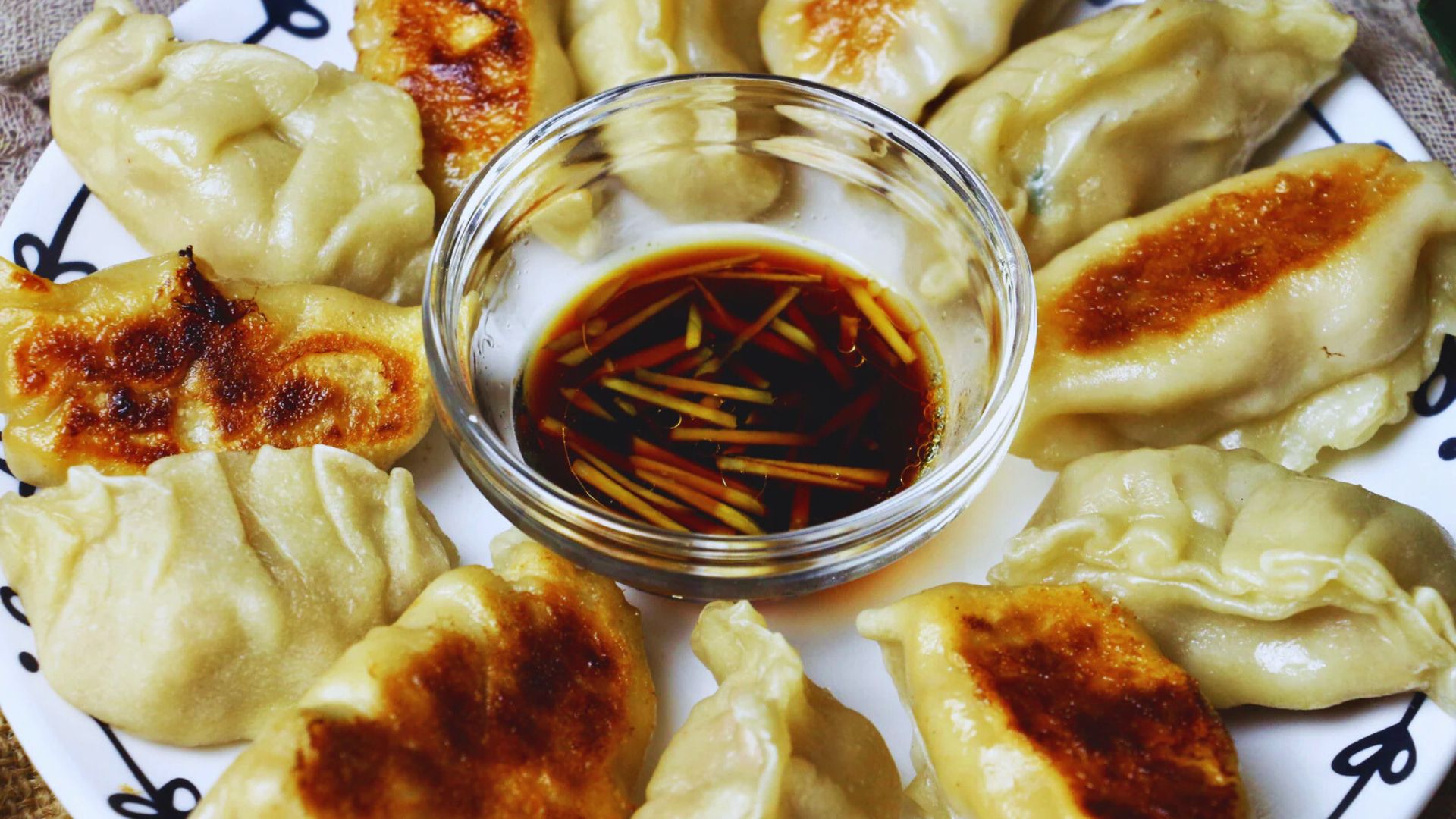 A plate of dumplings served with a side of dipping sauce.