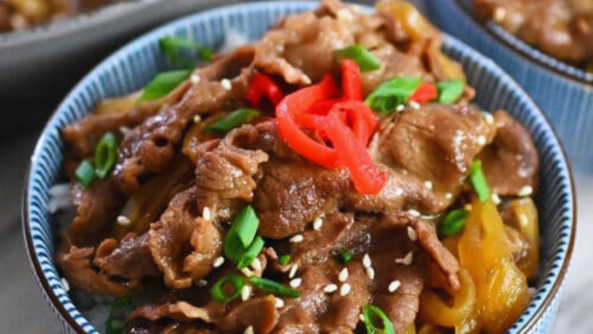 A bowl filled with beef and rice, garnished with vibrant red peppers.