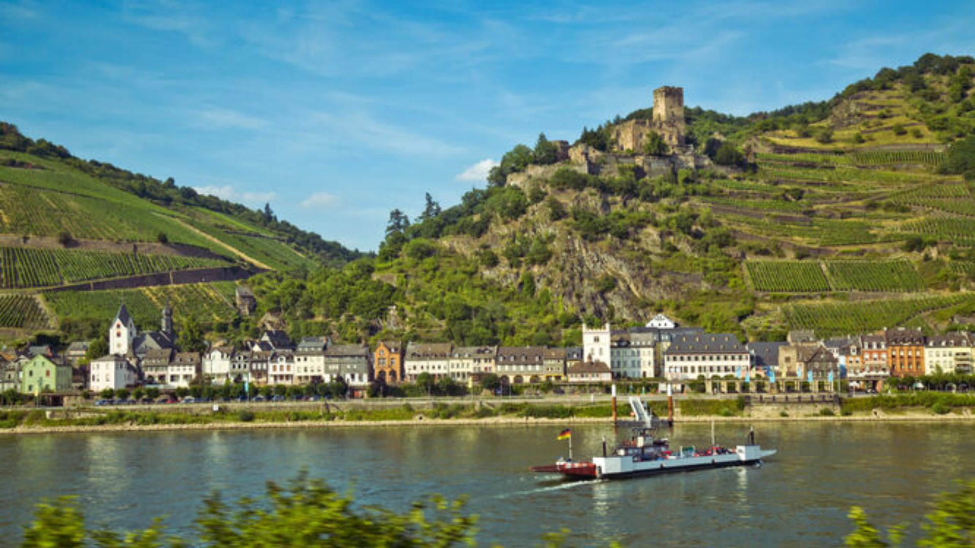 A boat glides down the river, with a town visible in the background under a clear sky.