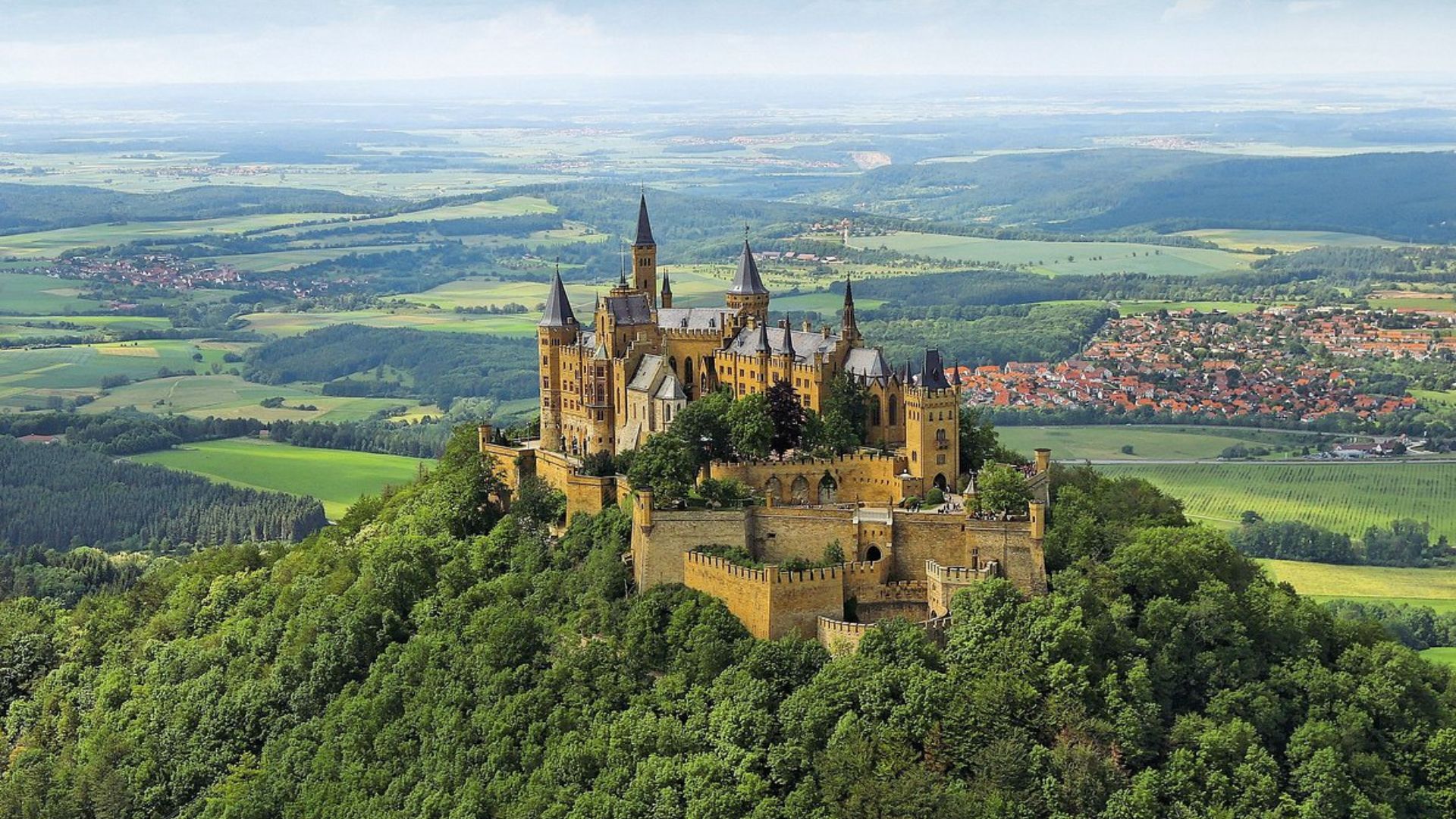 Hohenzollern Castle in Germany, a historic hilltop fortress surrounded by lush greenery and blue skies.