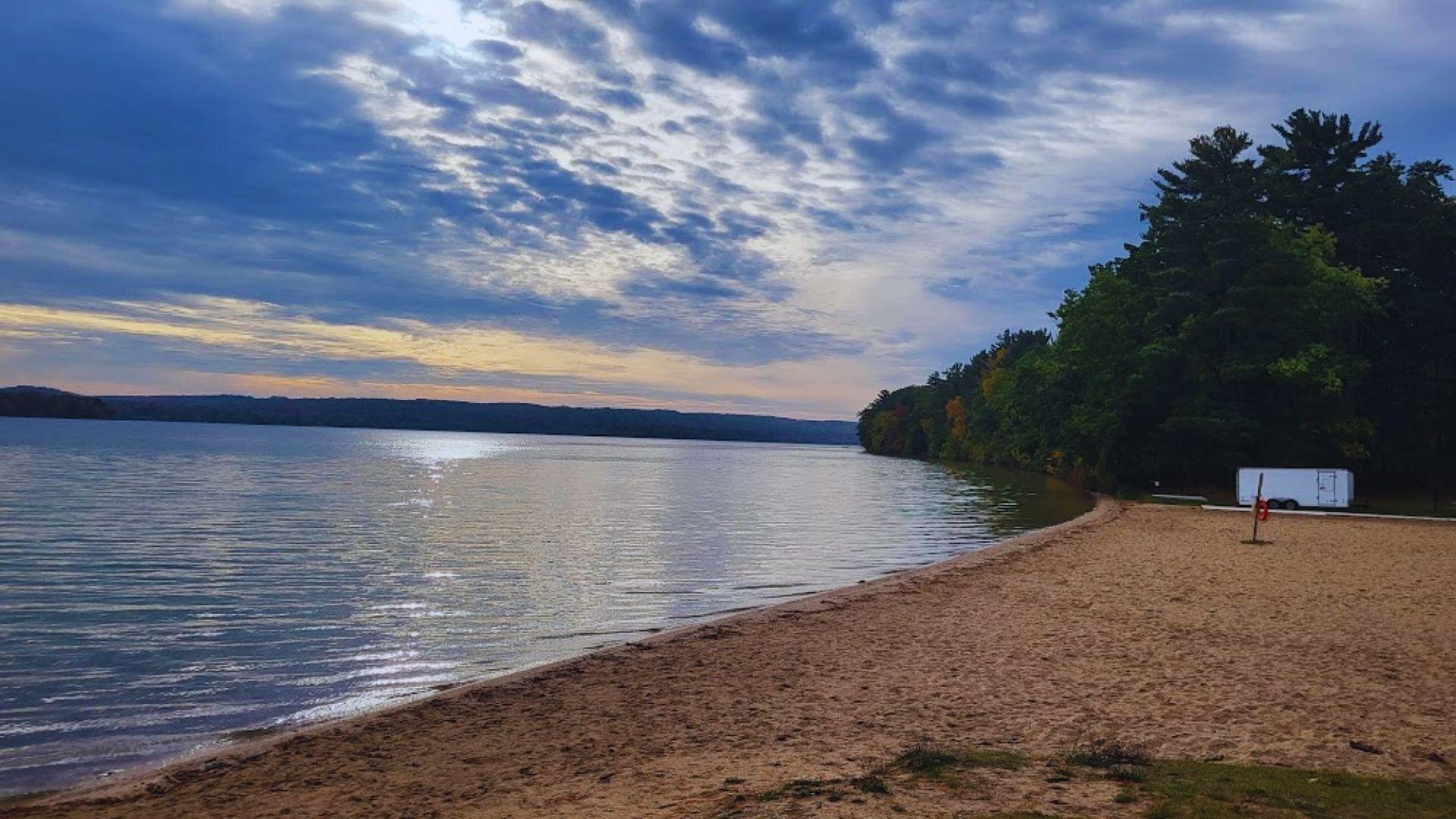 A sandy beach with a tranquil lake and lush trees in the background, creating a serene natural landscape.
n