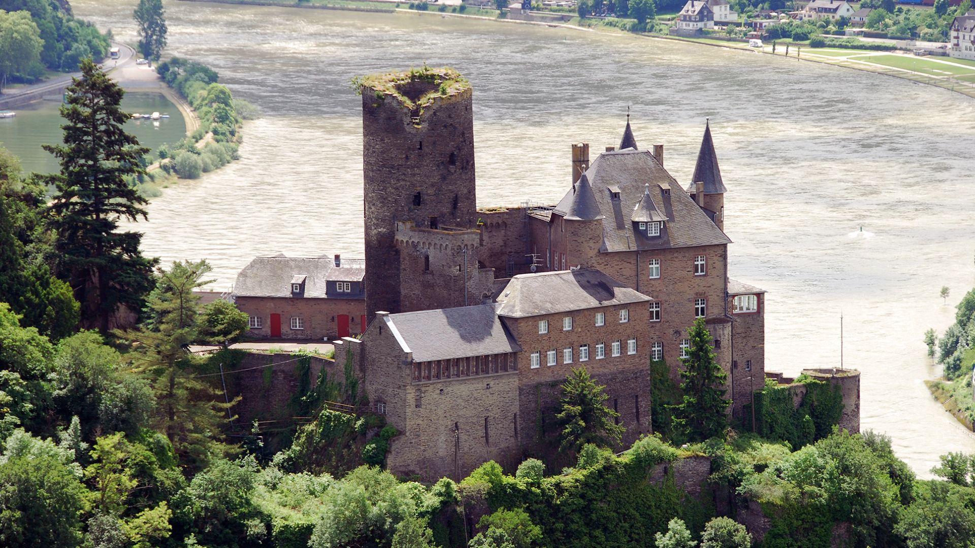 A majestic castle perched atop a green hill, surrounded by trees and a clear blue sky.
