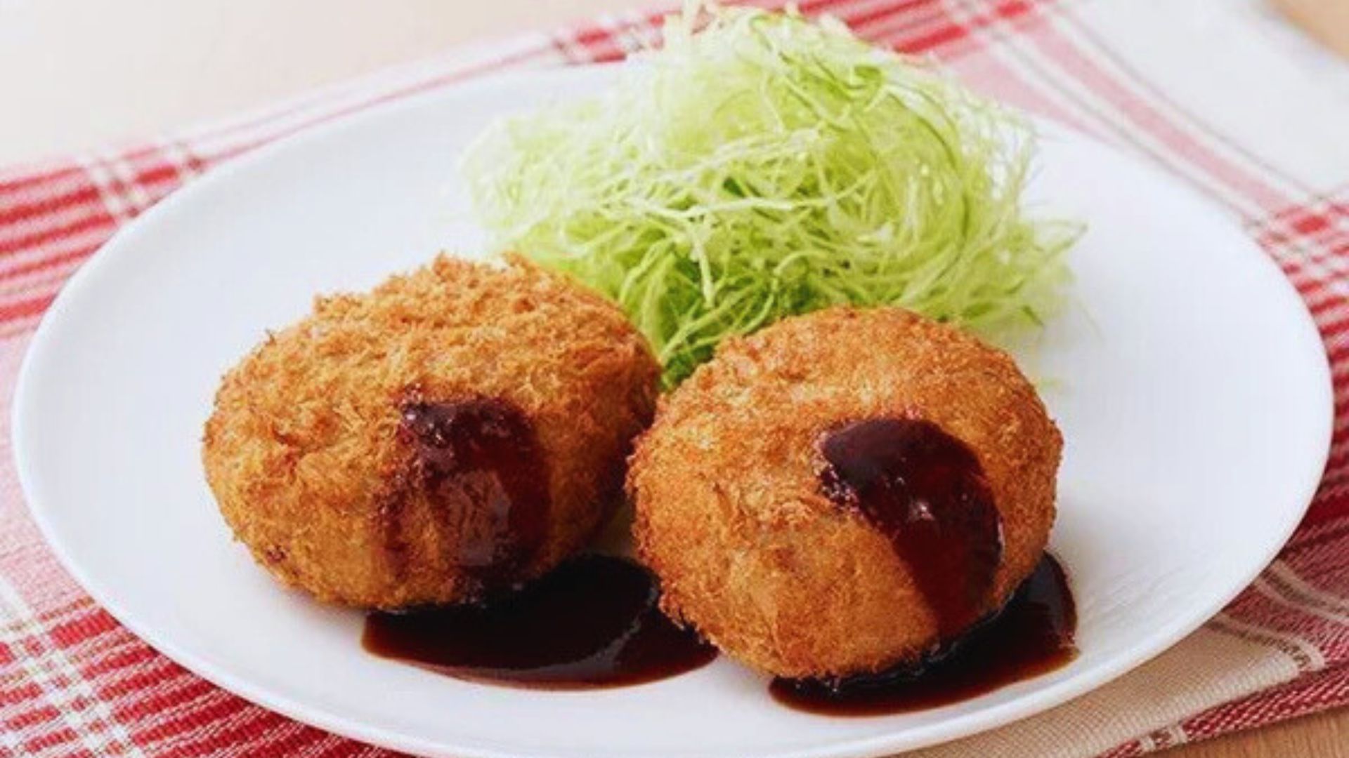 Two fried meatballs drizzled with sauce, served on a white plate.