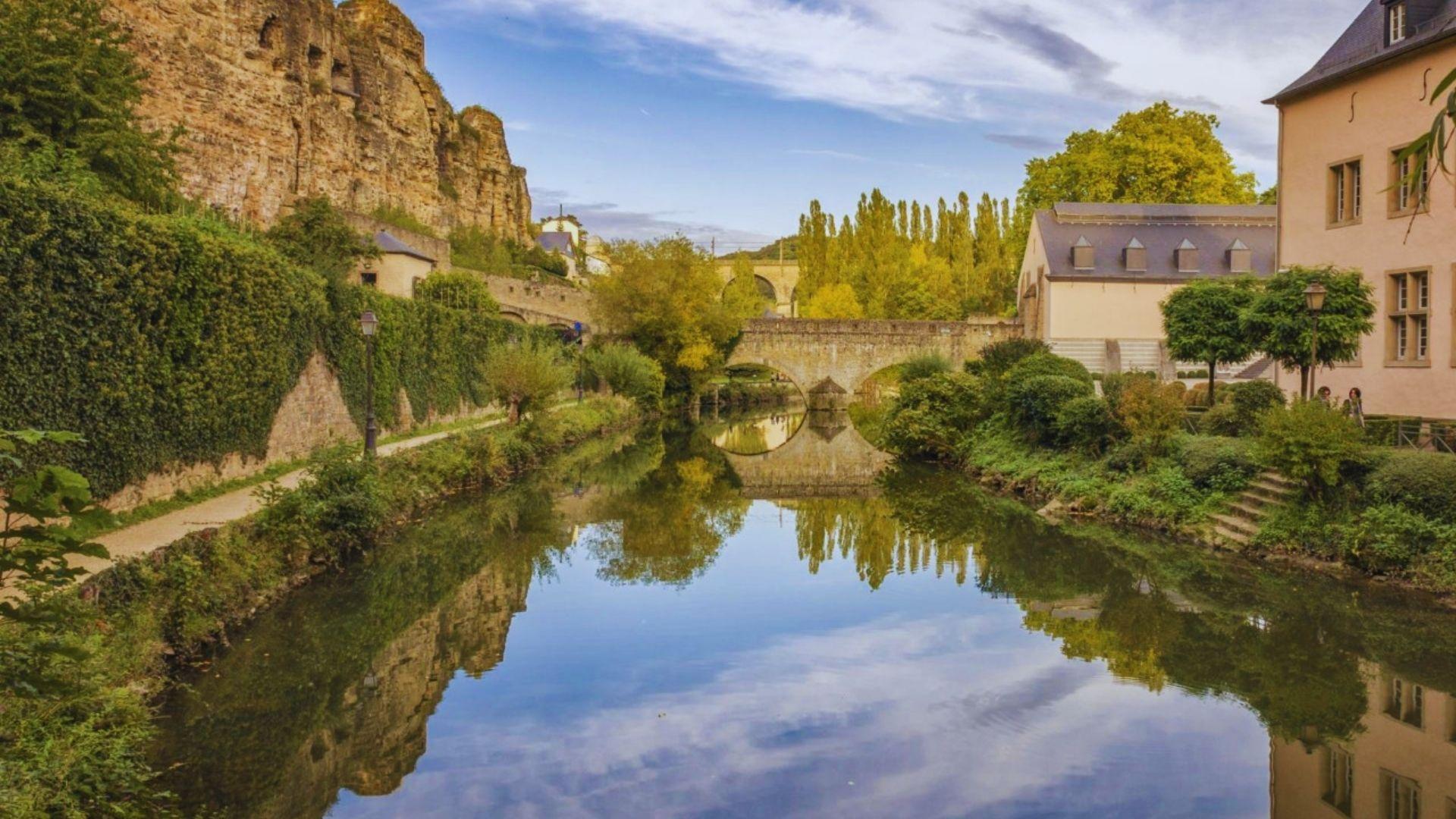A river flows through a quaint small town, surrounded by buildings and greenery.