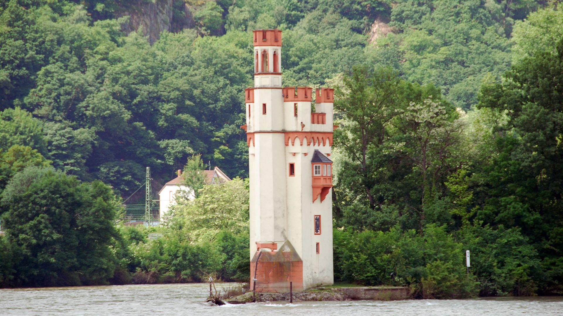 A tower stands on the riverbank, surrounded by trees in the background, creating a serene natural landscape.