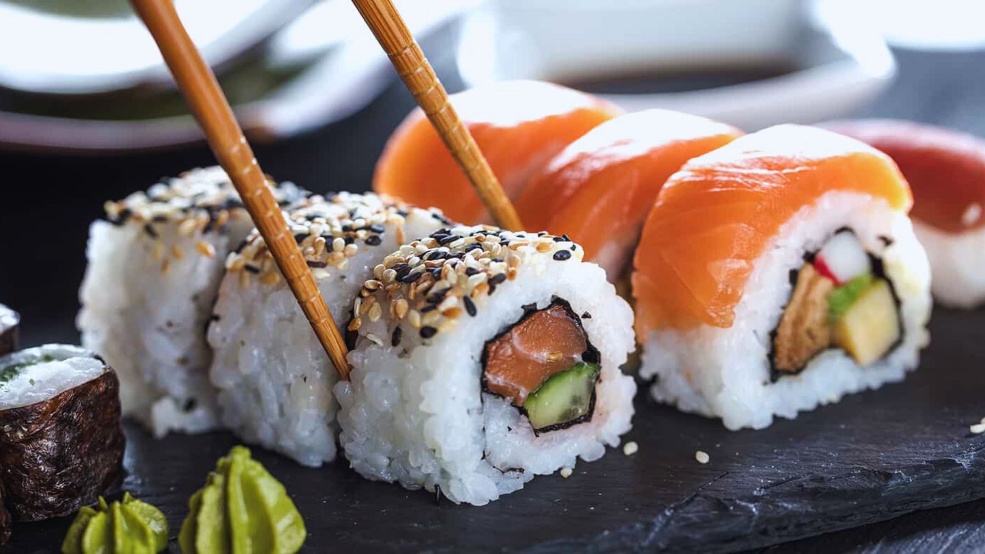 A selection of sushi arranged on a black slate, with chopsticks placed beside it for an elegant dining experience.