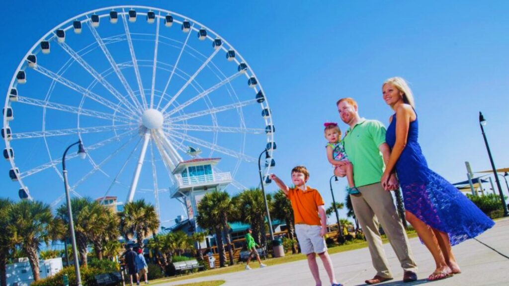 57 Myrtle Beach Attractions You Can’t Miss in 2026 A family smiles together in front of a colorful ferris wheel at an amusement park.