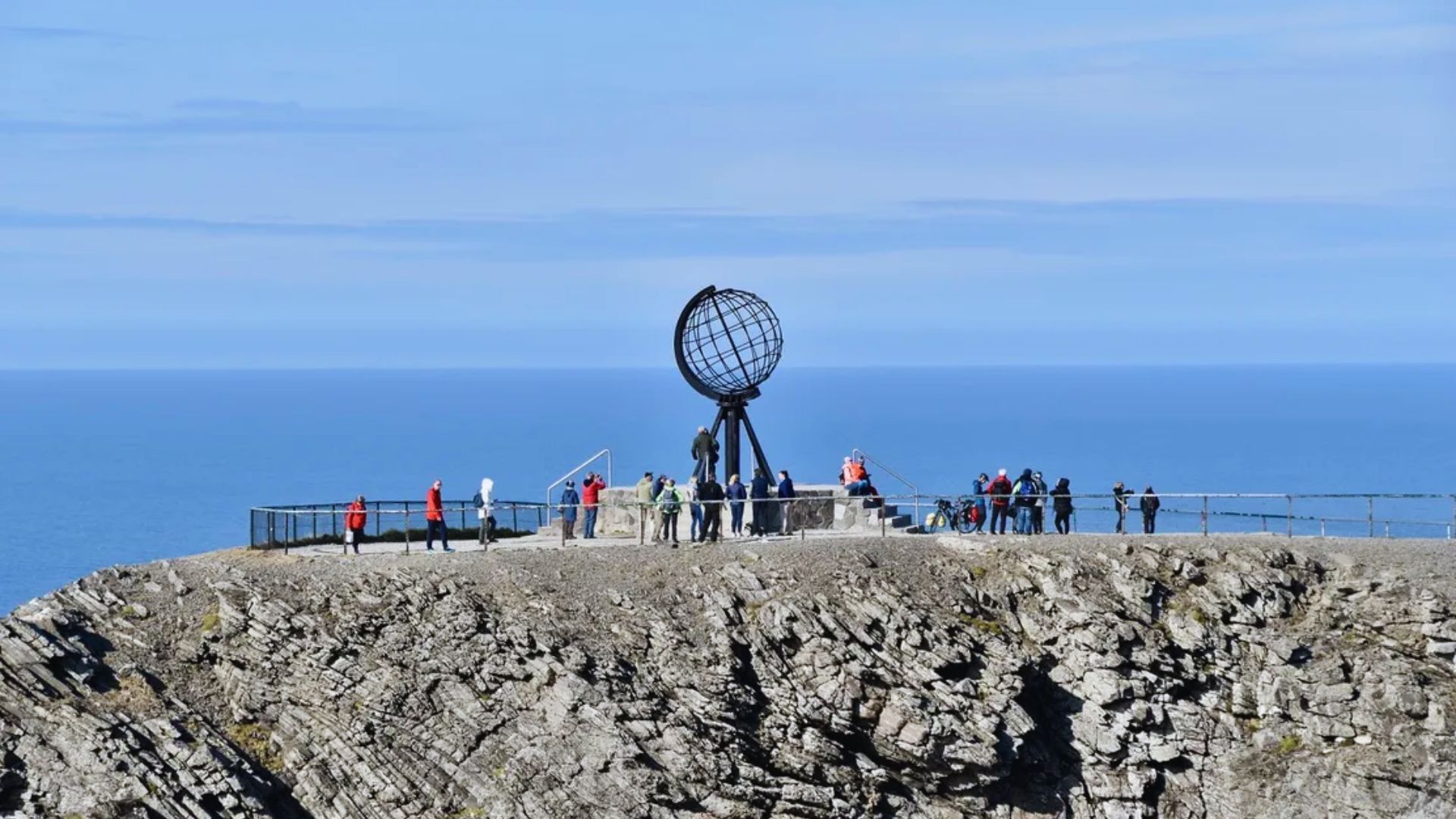 Several individuals are positioned on a cliff's edge, overlooking the expansive ocean and enjoying the scenic view.
