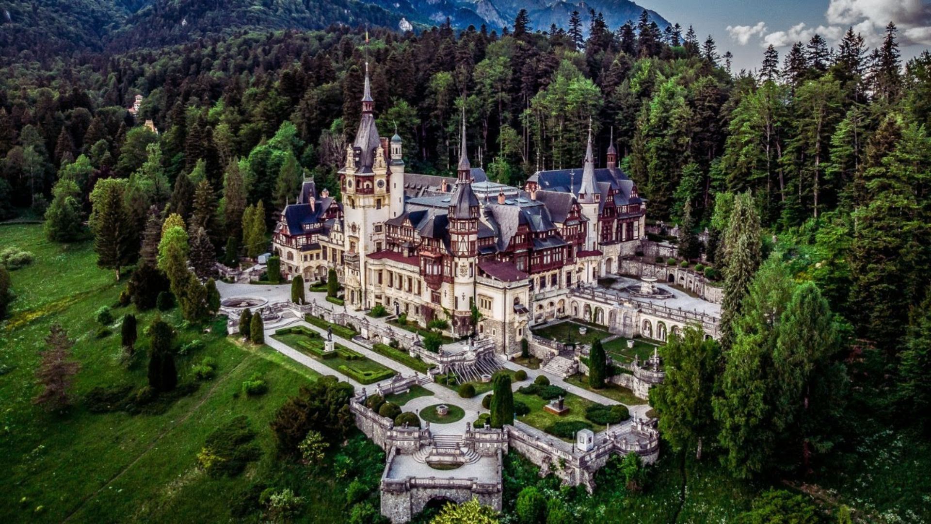 Aerial view of a castle surrounded by dense forest, showcasing its towers and greenery from above.