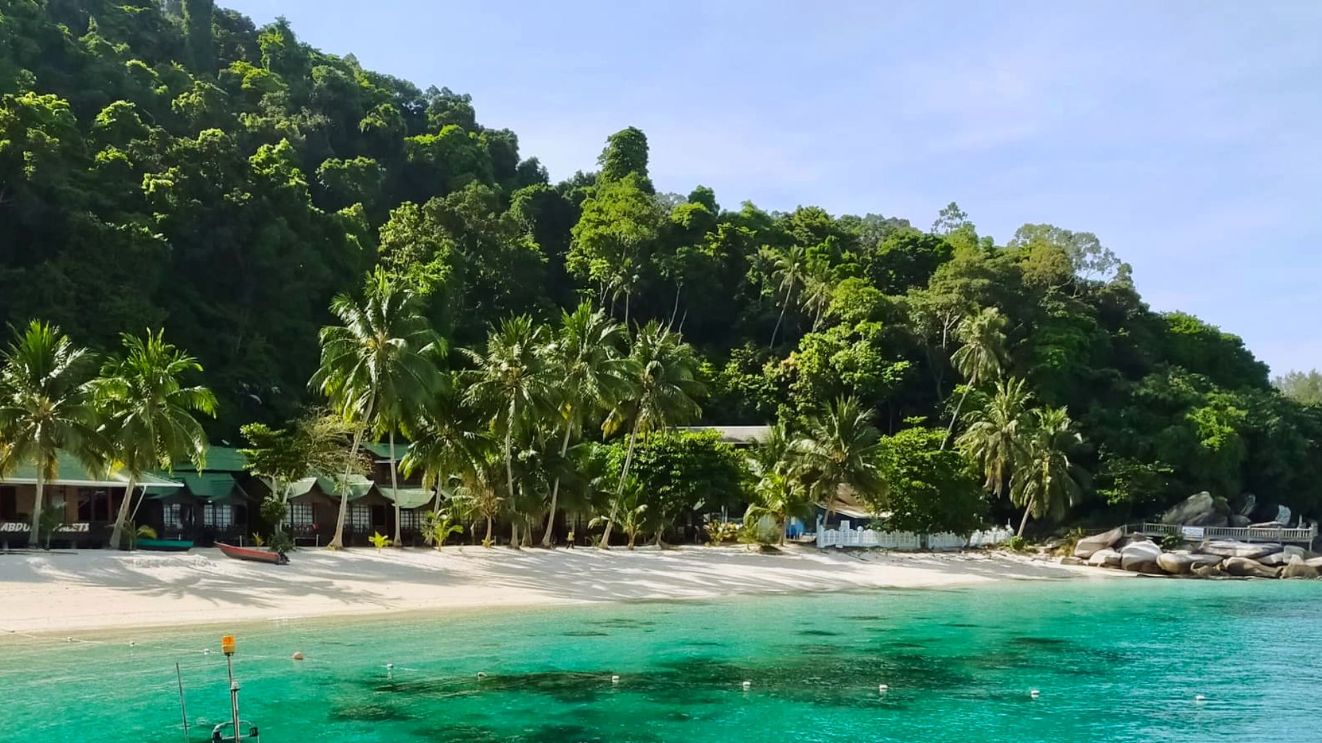 A scenic beach featuring a few houses and trees along the shoreline under a clear blue sky.