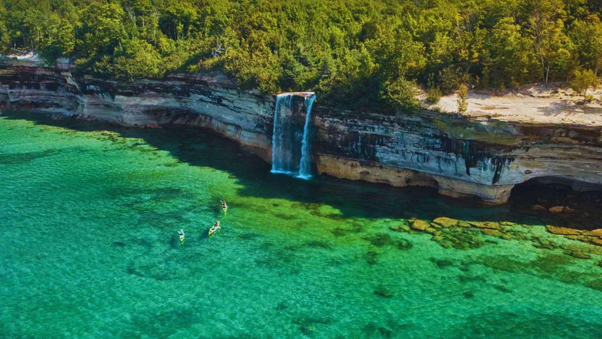 Aerial view of the stunning waterfalls at Pictured Rocks National Park, surrounded by lush greenery and rocky cliffs.