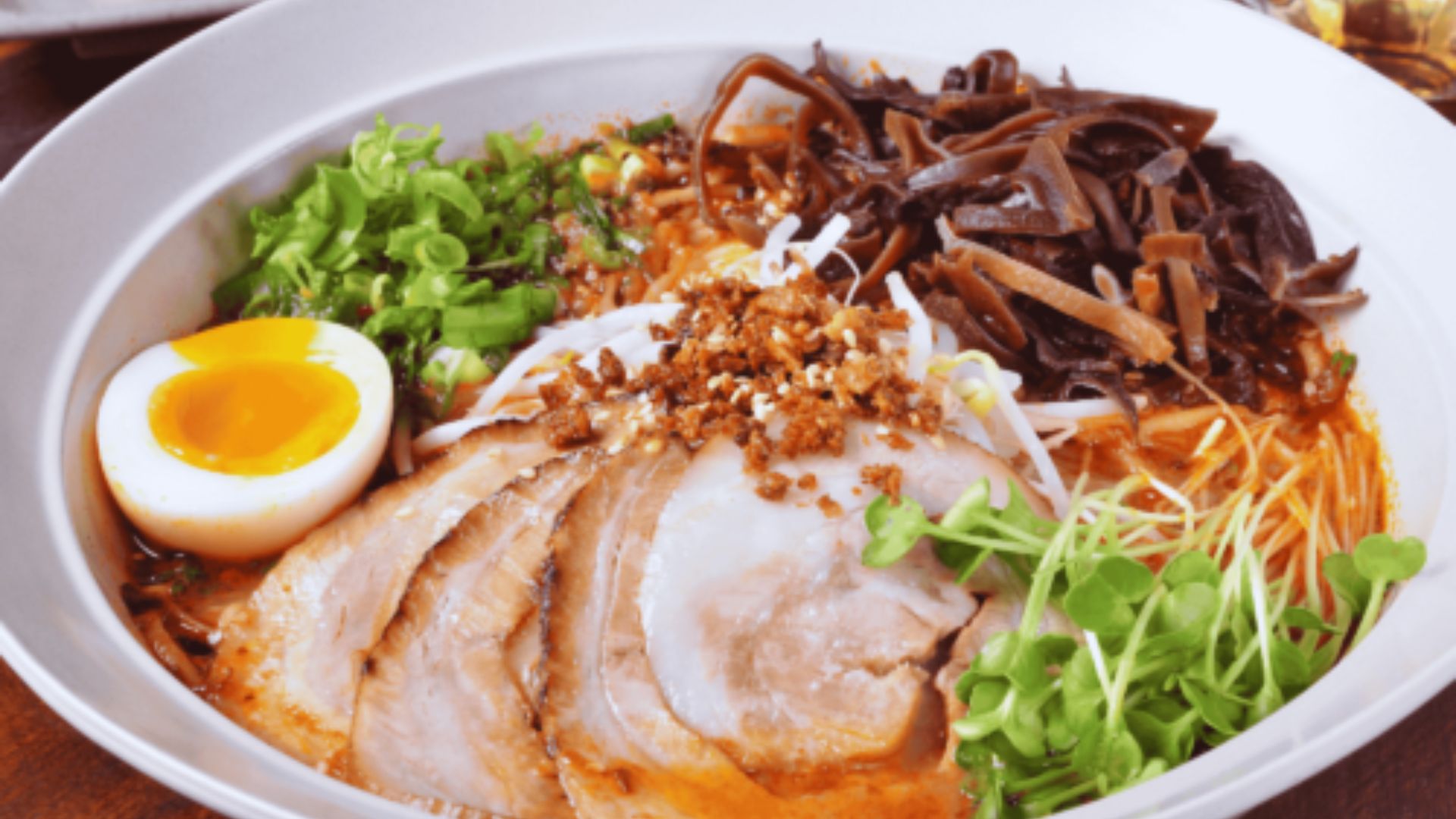 A bowl of ramen topped with slices of meat, soft-boiled eggs, and colorful vegetables.