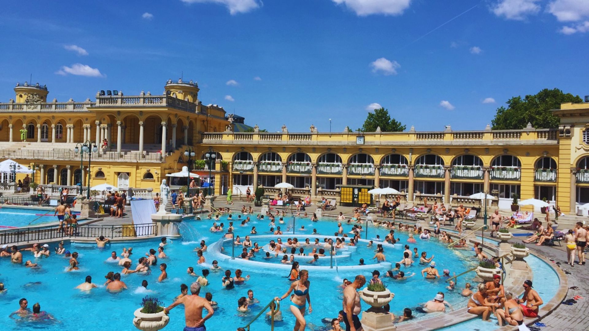 The thermal baths in Budapest featuring a large, inviting pool surrounded by ornate architecture and lush greenery.