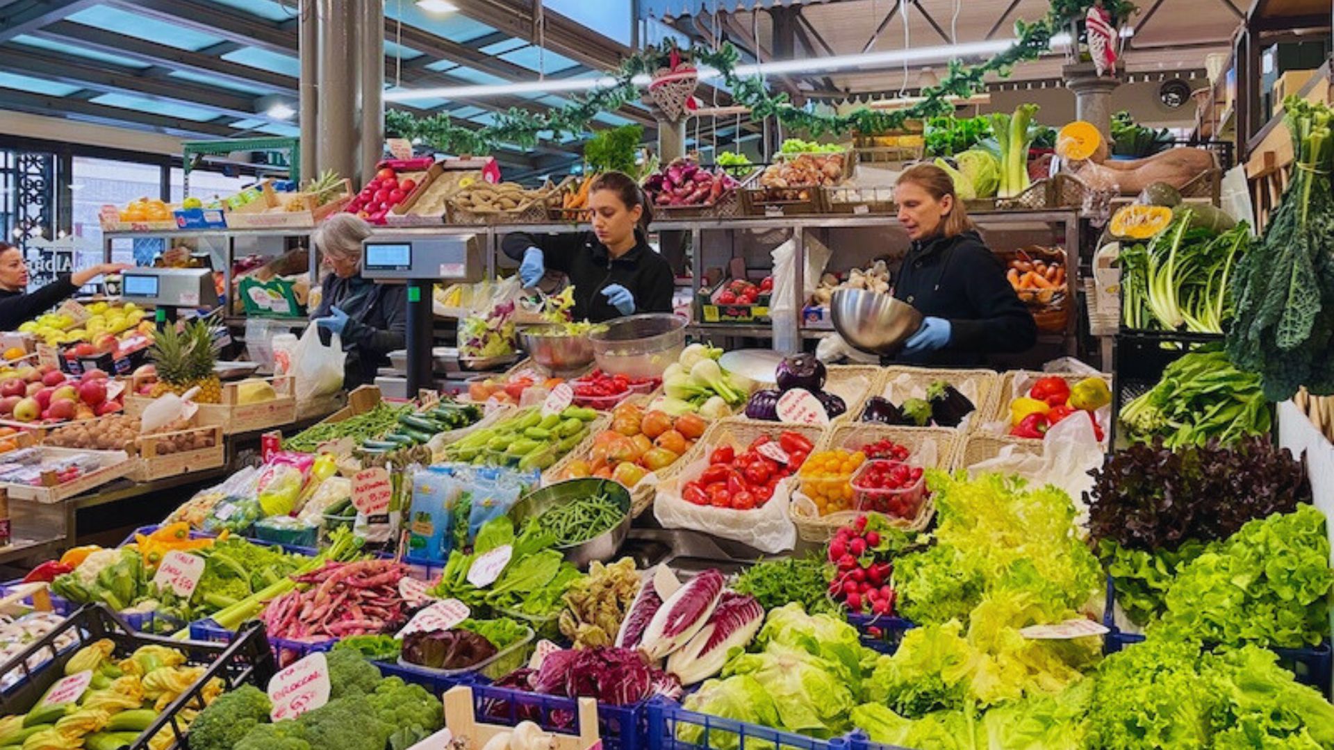 A vibrant market filled with shoppers exploring stalls of fresh produce, including fruits and vegetables.