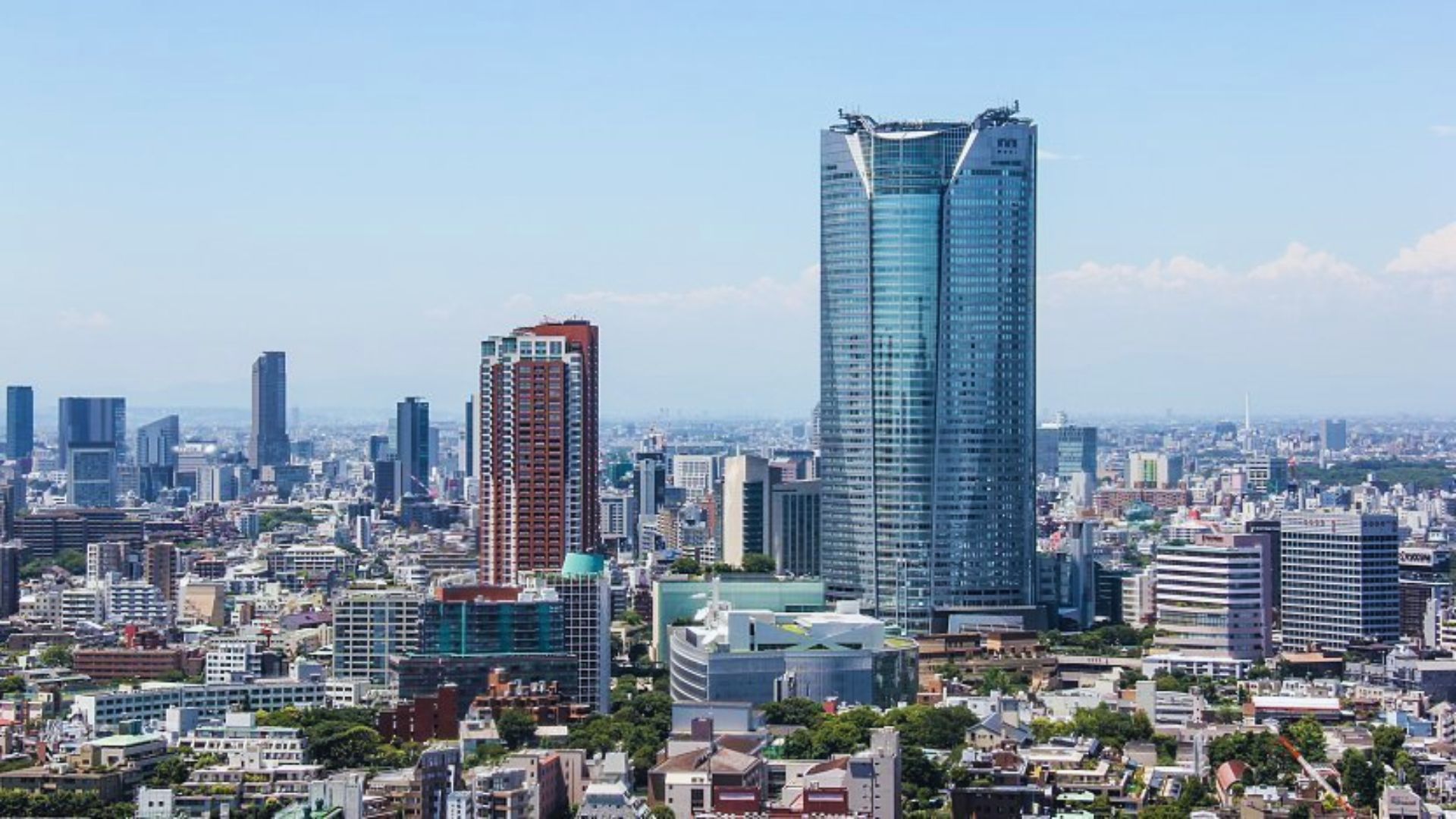 Aerial view of the Tokyo skyline, showcasing skyscrapers and urban landscape under a clear blue sky.