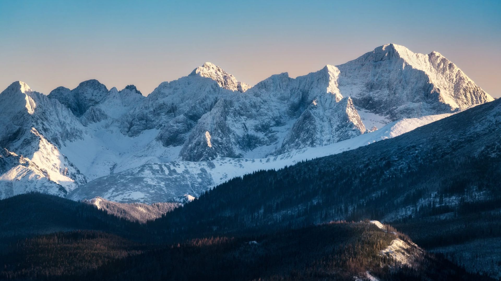 . A panoramic view of a mountain range featuring majestic snow-capped peaks against a clear blue sky.