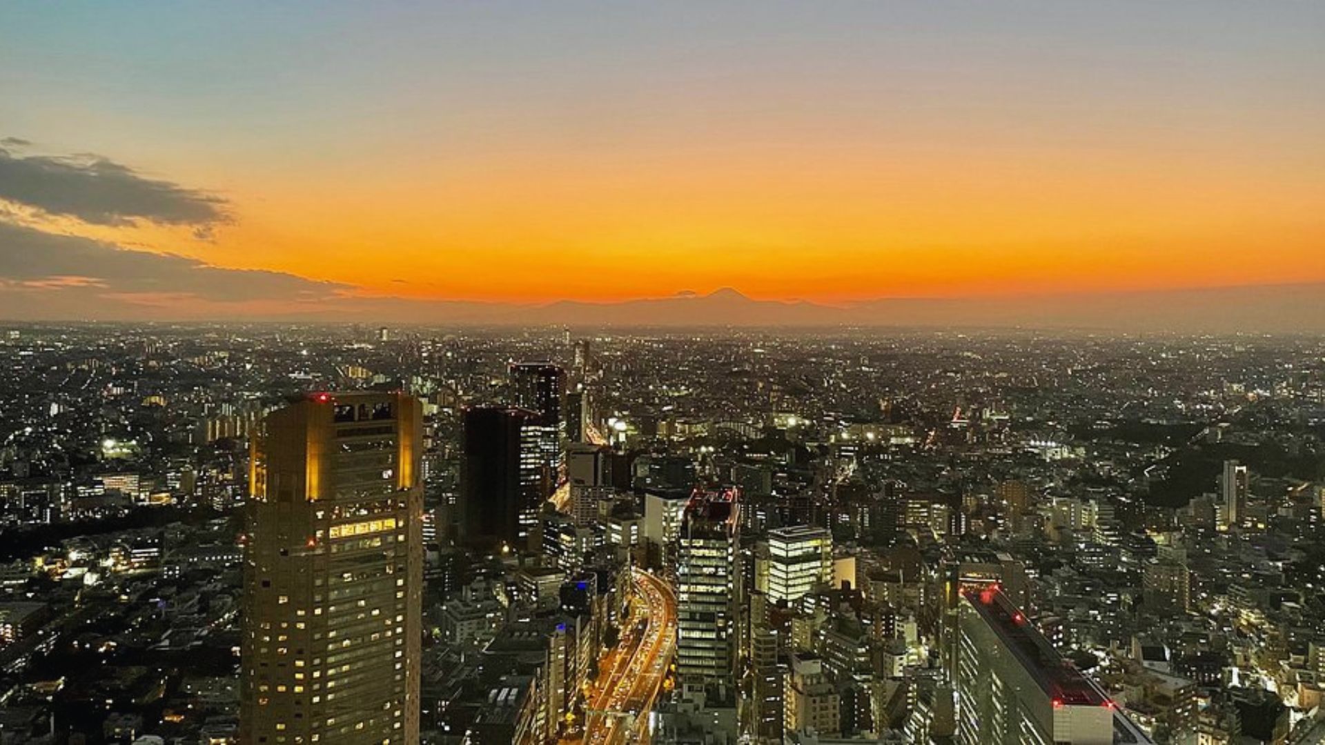 City skyline at sunset, with the sun setting behind the buildings, casting a warm glow over the horizon.