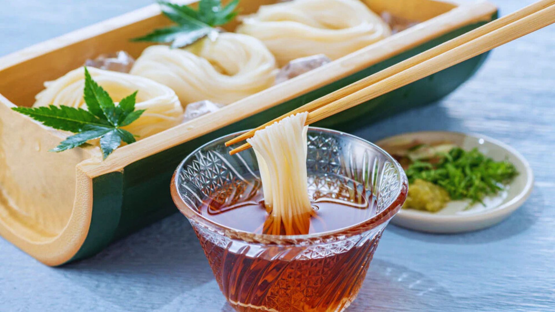 A bowl of steaming noodles with chopsticks and a glass of tea on a rustic table.