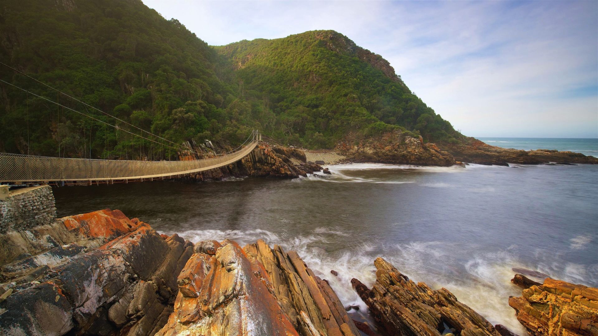Suspension bridge spanning the ocean in Cape Town, South Africa, with scenic views of the coastline and mountains.