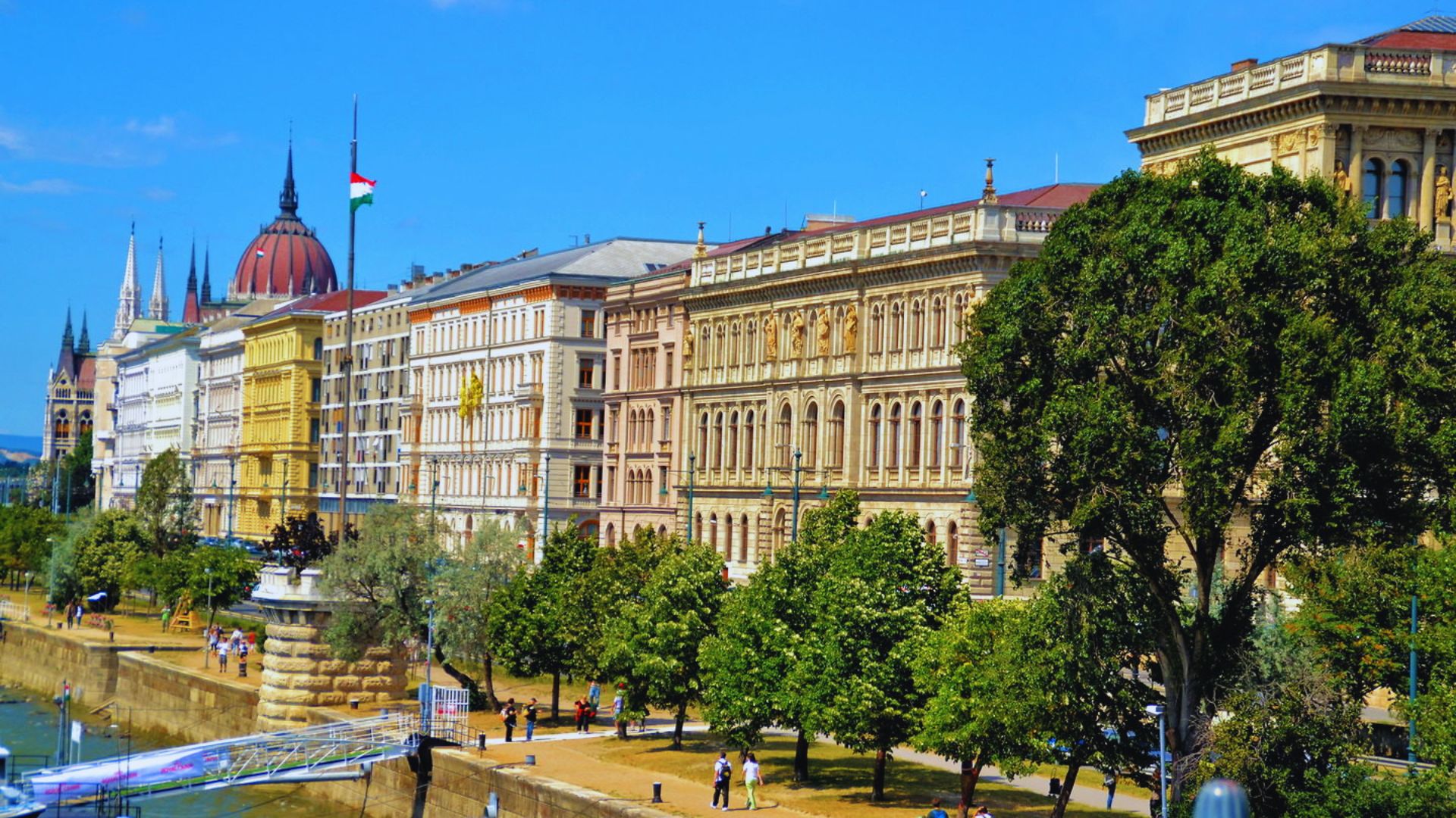 The Budapest riverfront features buildings and people enjoying the scenic view along the water's edge.