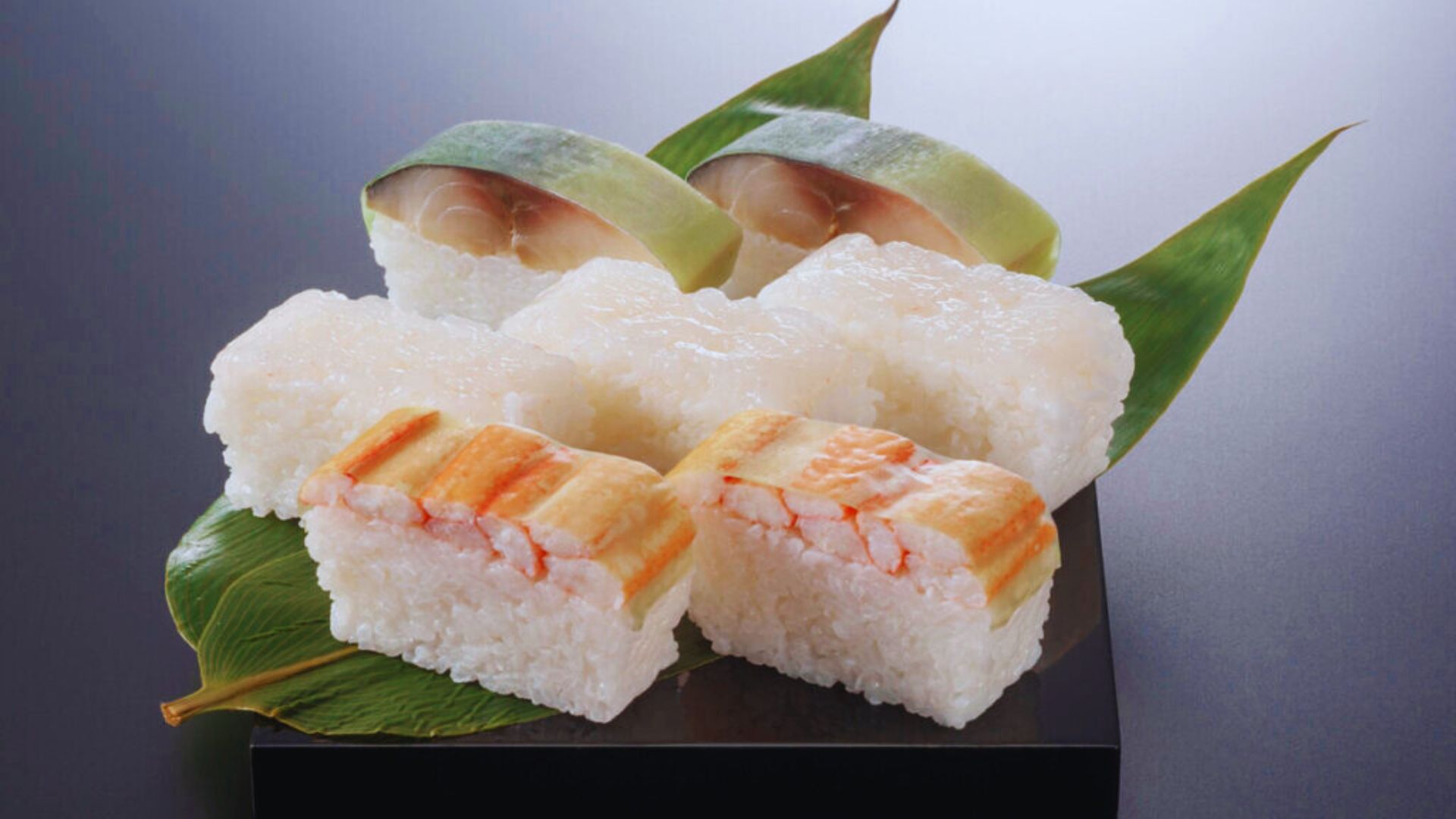 Sushi featuring shrimp and assorted vegetables arranged on a sleek black plate.
