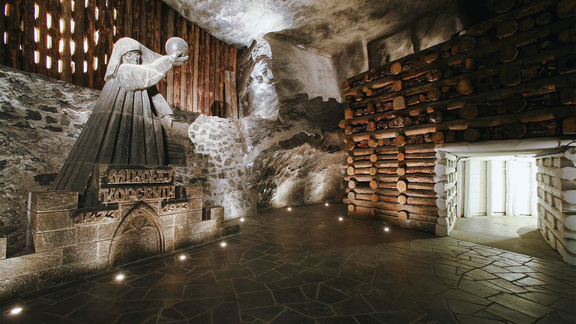 Inside a cave, a statue of a woman stands amidst rocky walls, illuminated by soft, natural light.