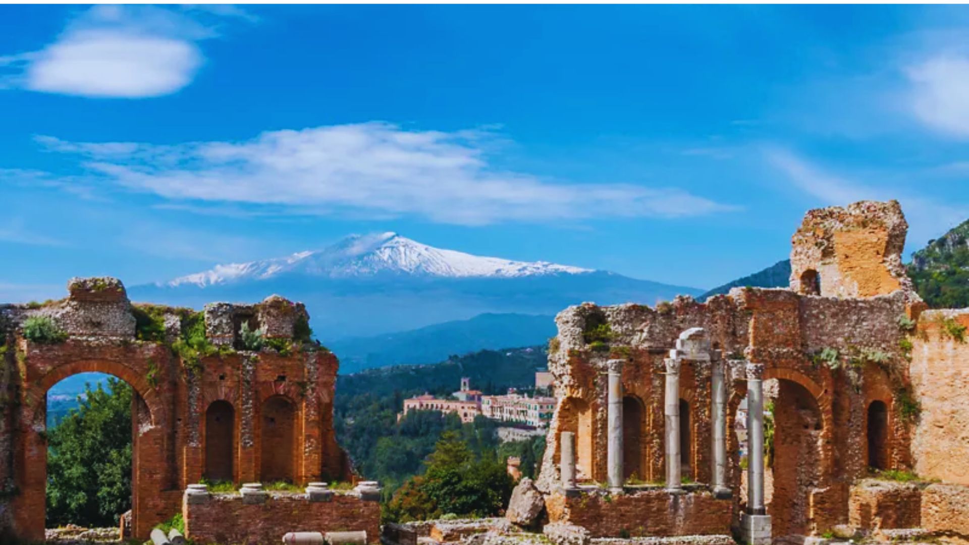Ruins of ancient Taranto, Sicily, with a volcano in the background, showcasing historical architecture and natural beauty.
