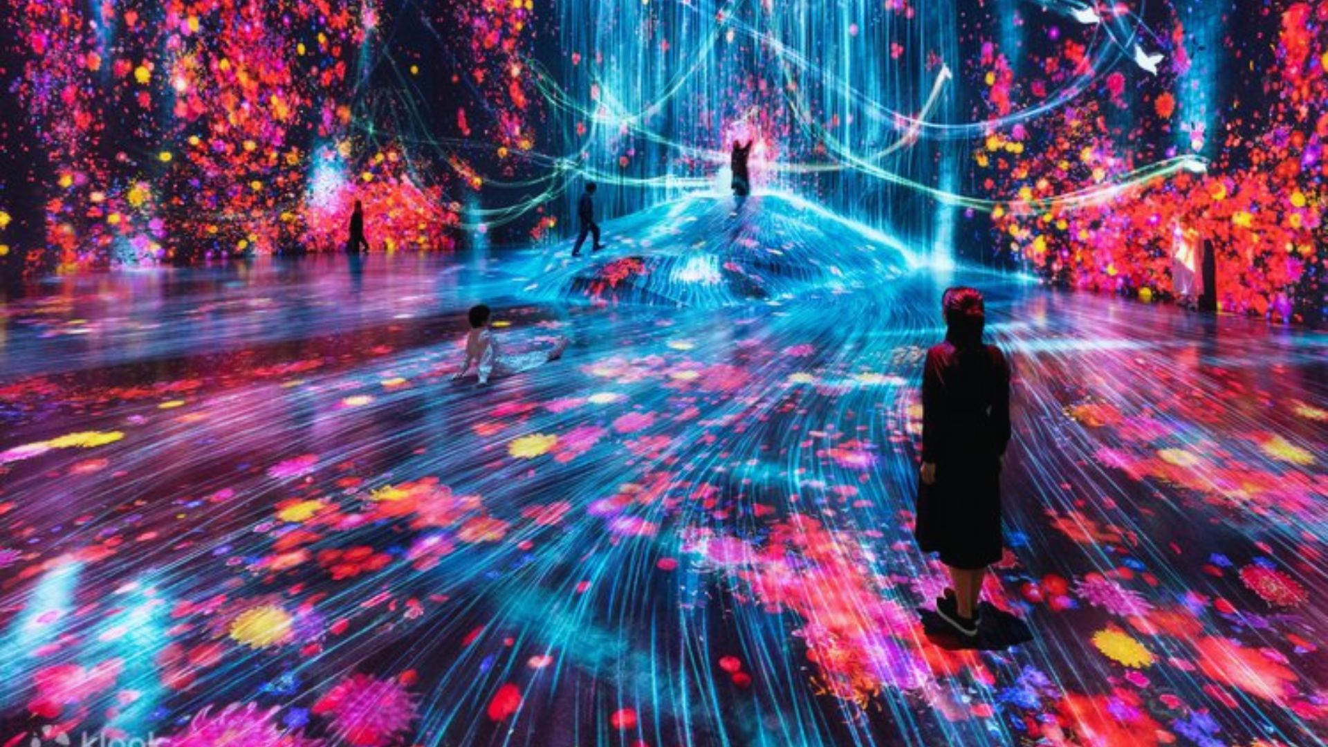 A man stands before a vibrant light show, illuminated by a spectrum of colors in a dynamic display.