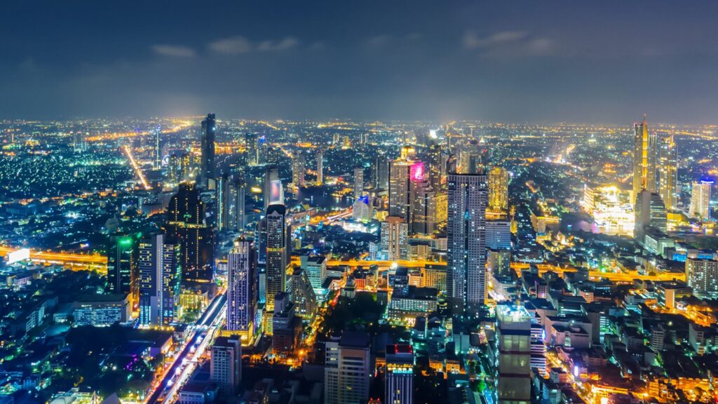 Bangkok's city skyline illuminated at night, showcasing tall buildings and vibrant lights against a dark sky.