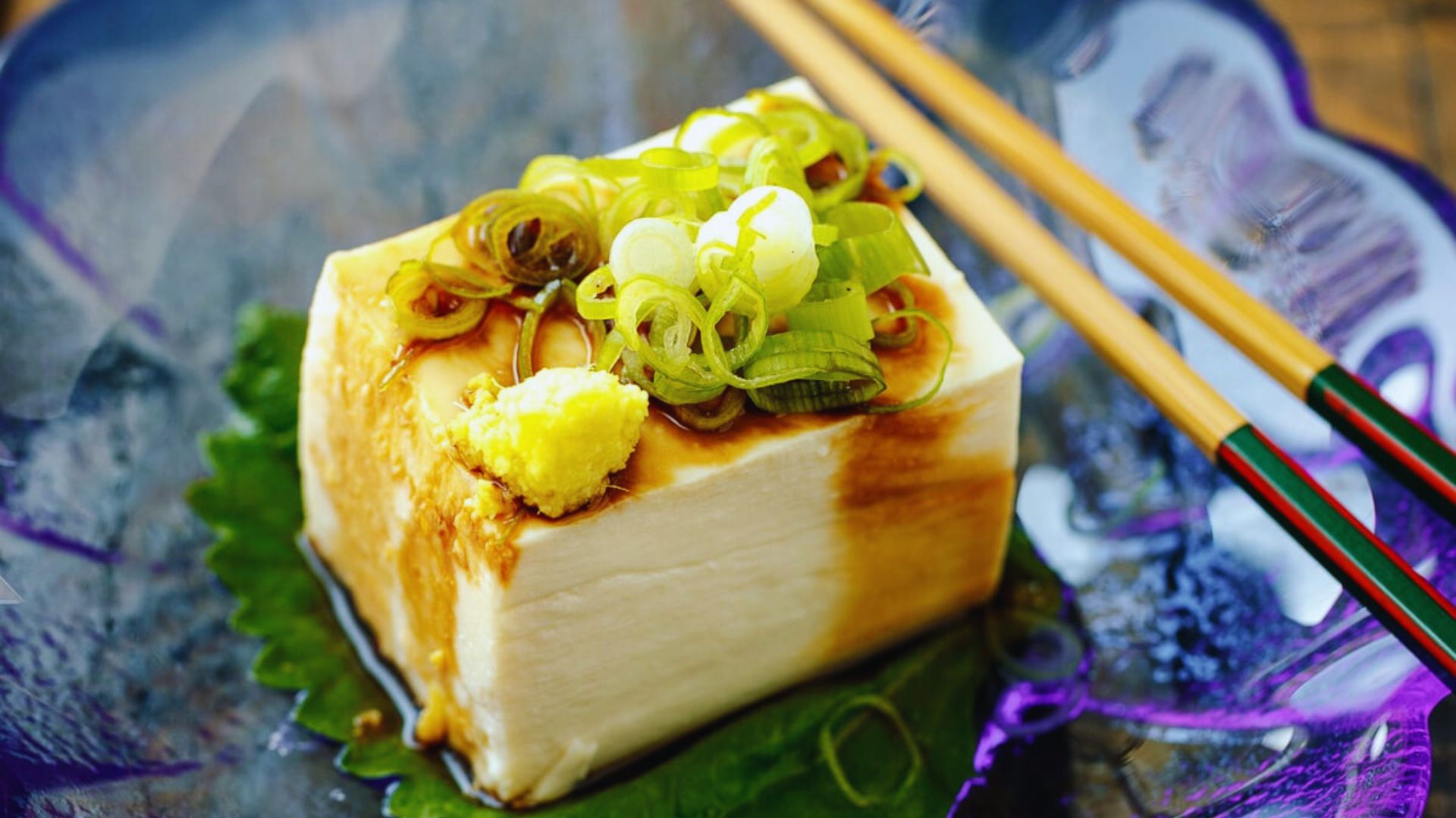 A piece of tofu topped with chopsticks, showcasing a simple Asian culinary presentation.