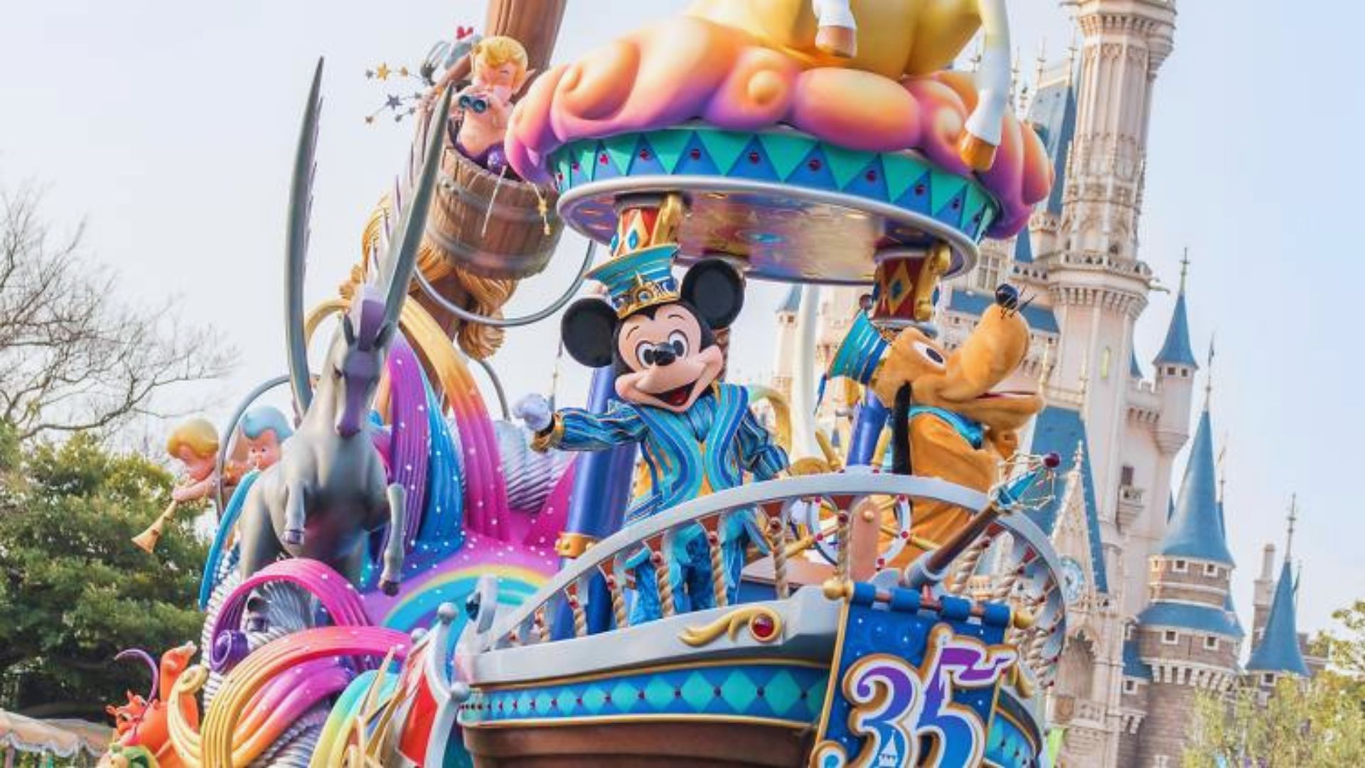 A colorful parade float featuring Mickey Mouse and various other beloved characters, surrounded by festive decorations.