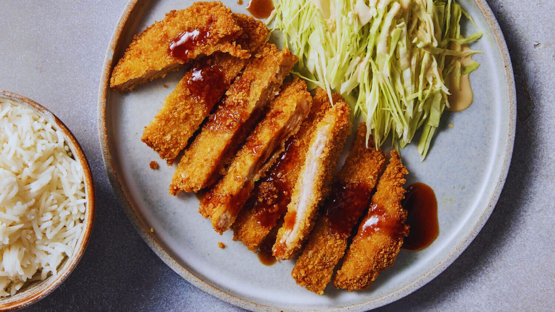 A dish of rice served with two crispy chicken cutlets on a white plate.