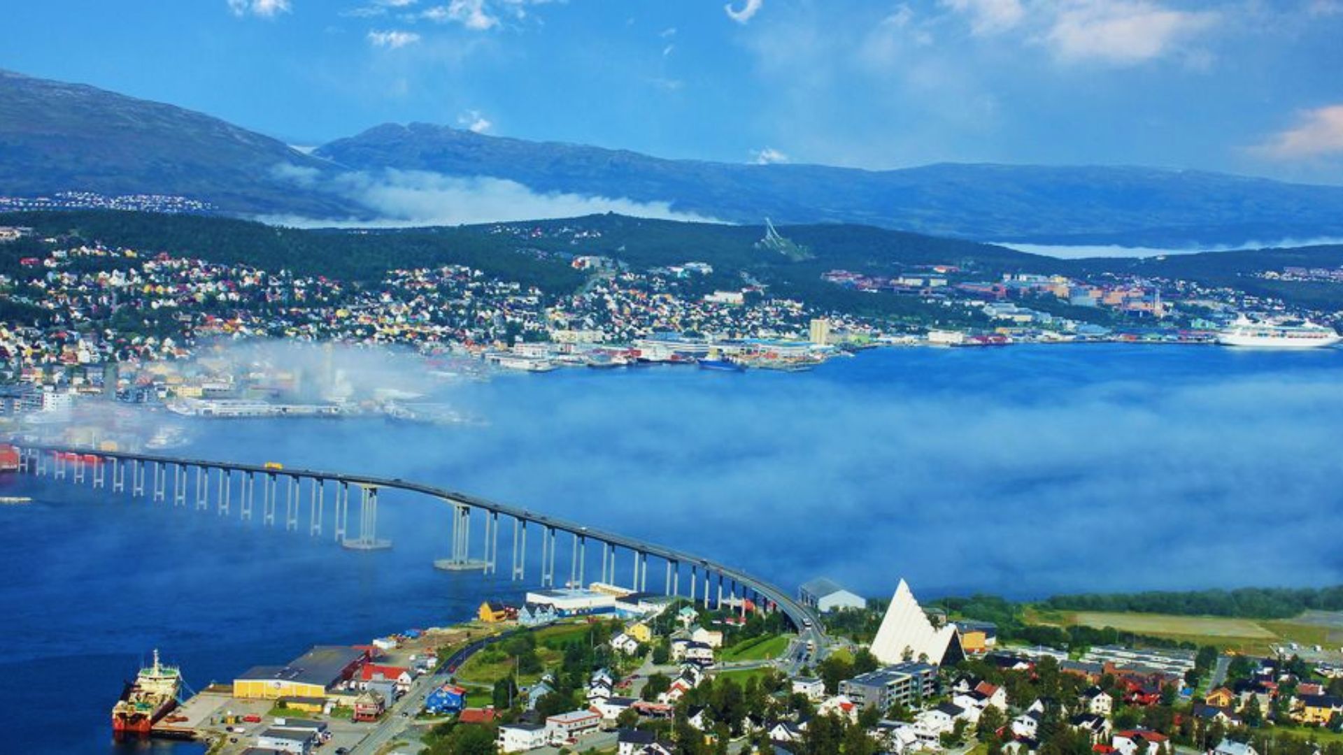 A scenic view of a city with a bridge spanning over a tranquil fjord, reflecting the surrounding landscape.