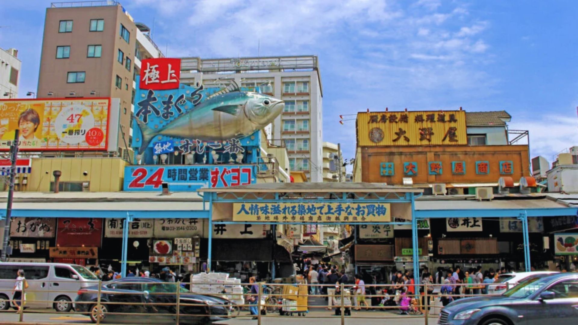 A bustling street scene featuring cars and signs in front of a vibrant fish market.