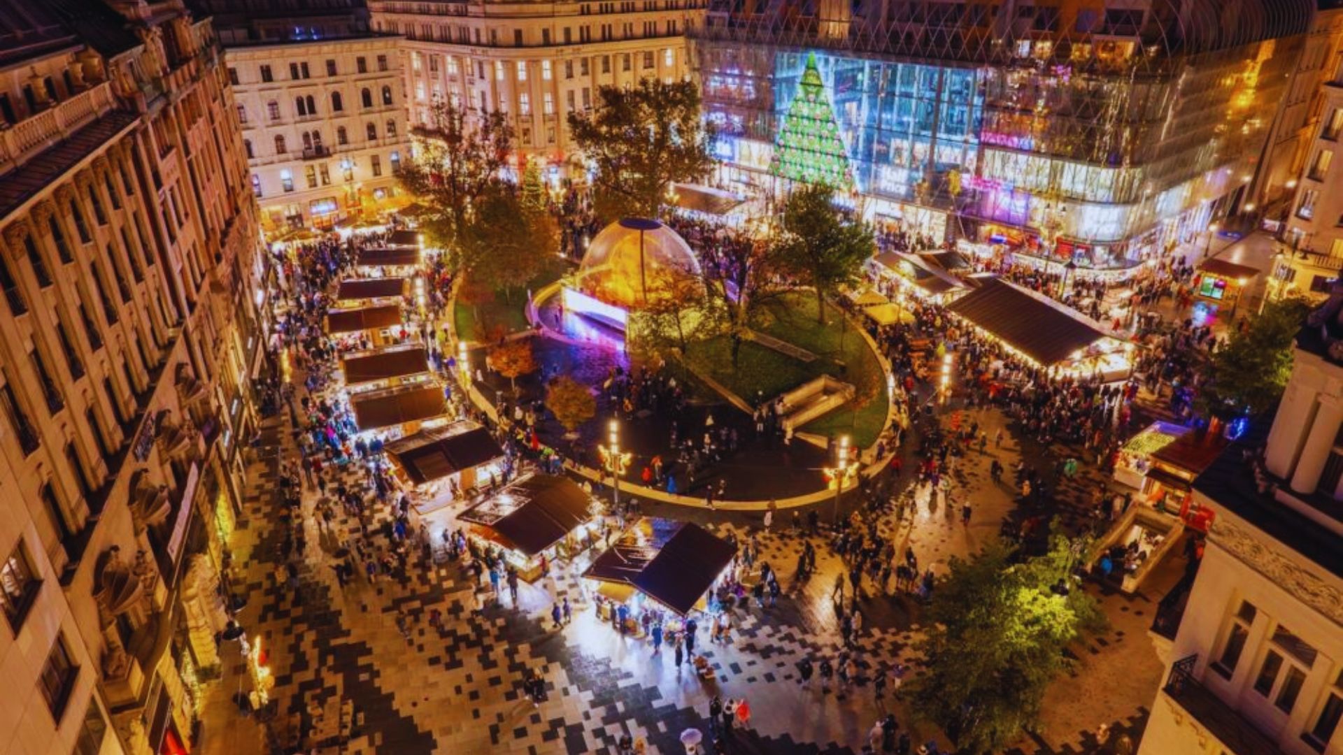Aerial view of a bustling Christmas market in a city, featuring festive stalls and twinkling lights.