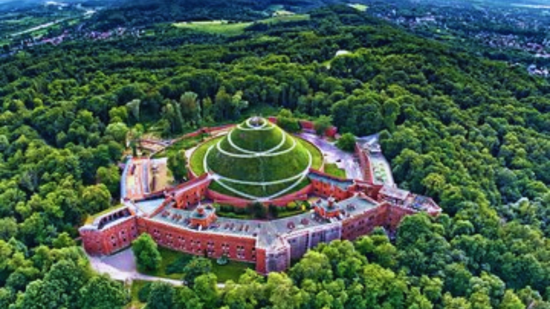 A vast greenhouse stands prominently in a lush forest, showcasing its size amidst the surrounding trees.