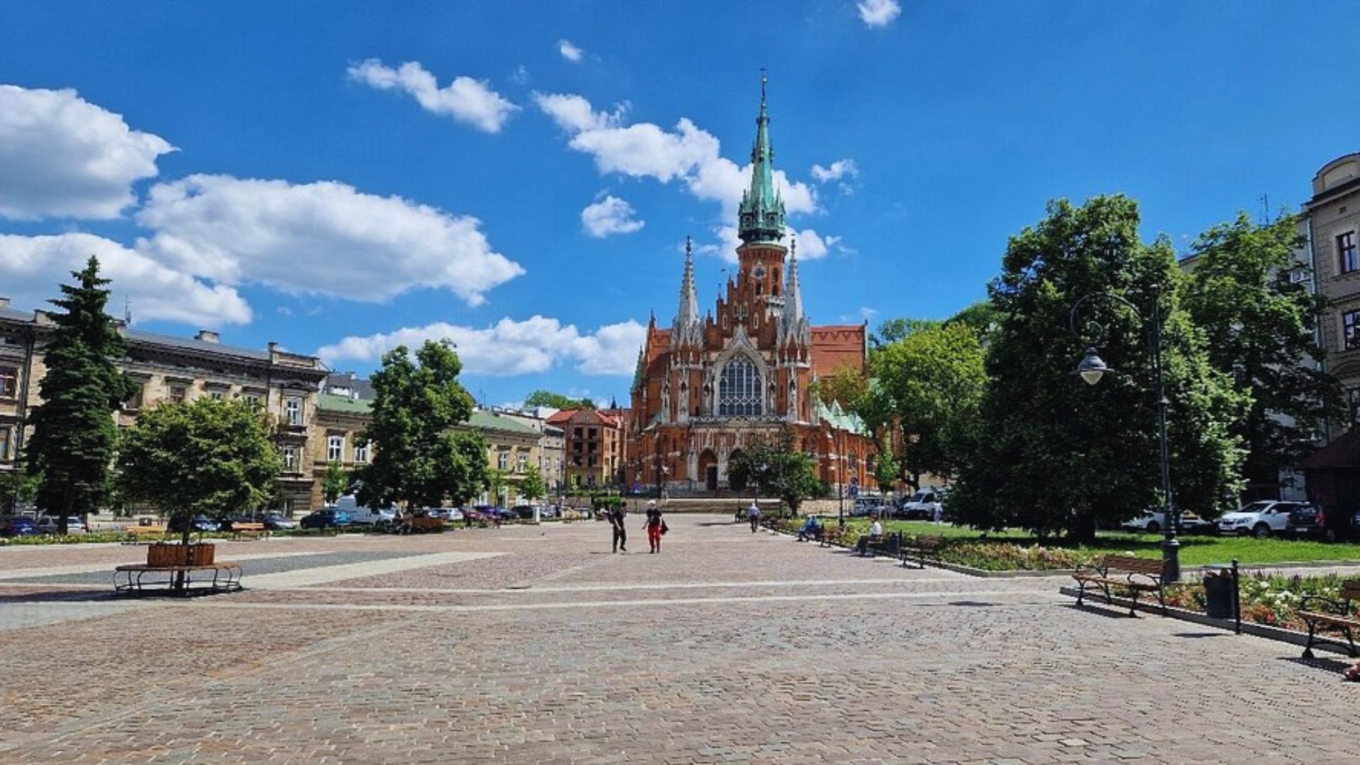 A bustling city square with people, featuring a prominent church in the background against a clear blue sky.