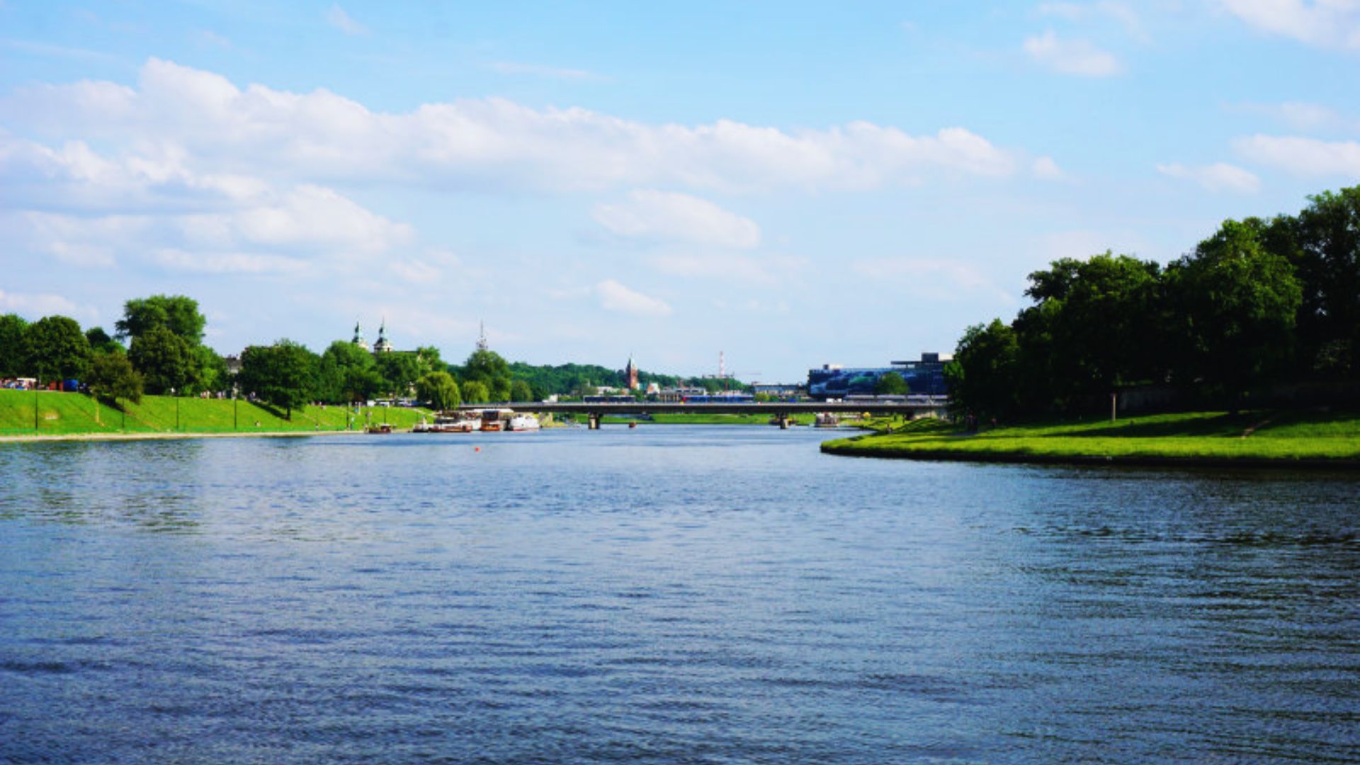 A serene body of water reflecting the sky, surrounded by lush greenery and distant hills.