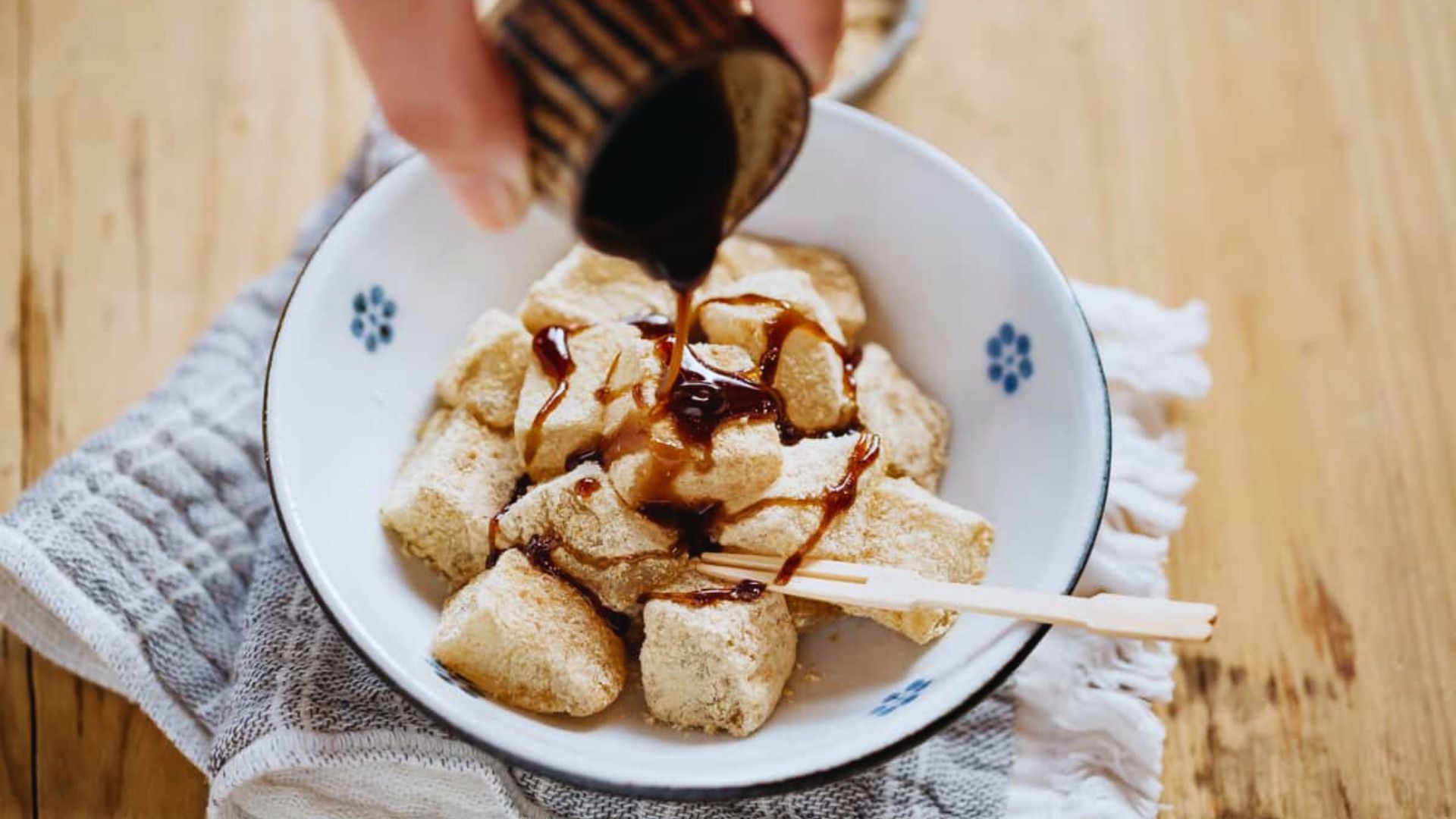 A person pours syrup over a bowl of food, enhancing its flavor and presentation.