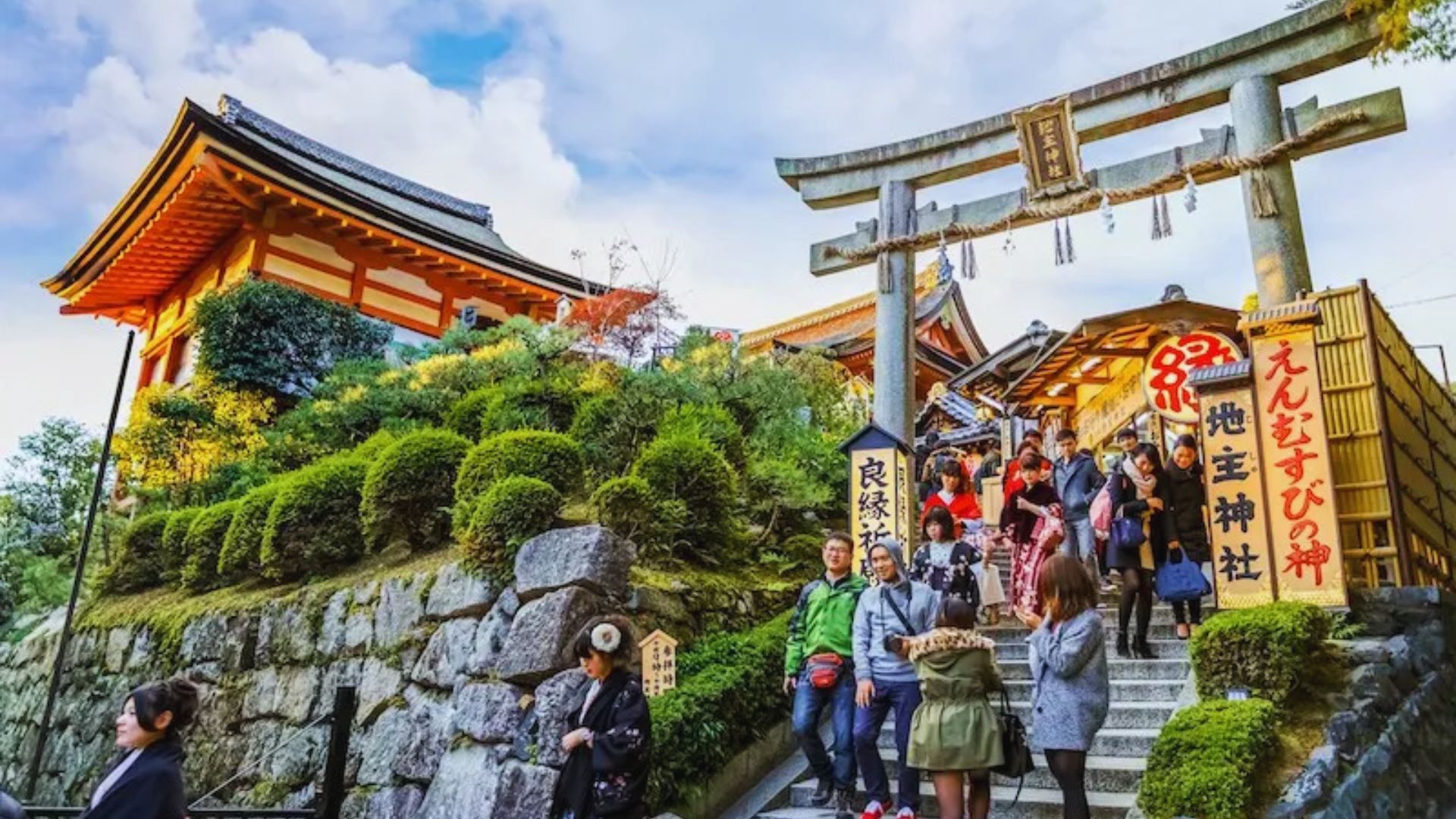 Tourists gather at the entrance of a traditional shrine in Kyoto, Japan, surrounded by lush greenery and historic architecture.