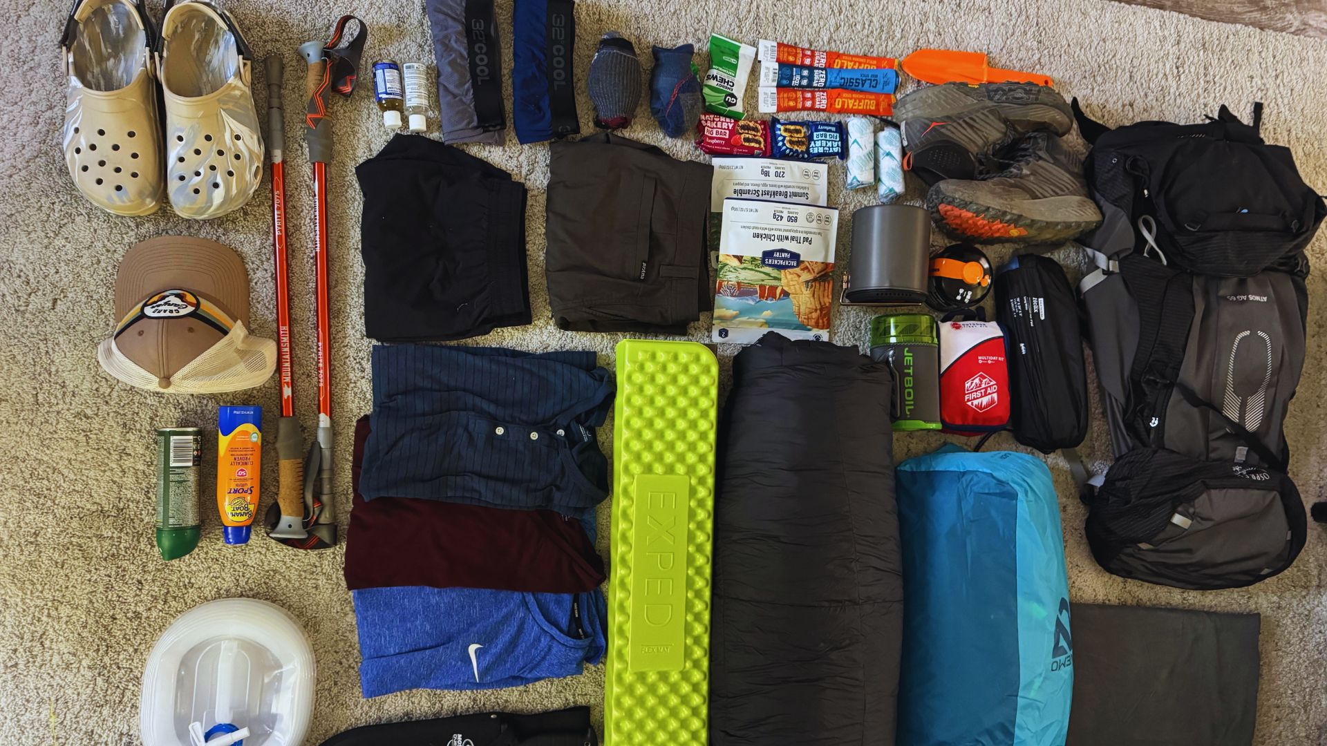 A bag overflowing with various items, including shoes, a backpack, and multiple sleeping bags and pads for outdoor use.