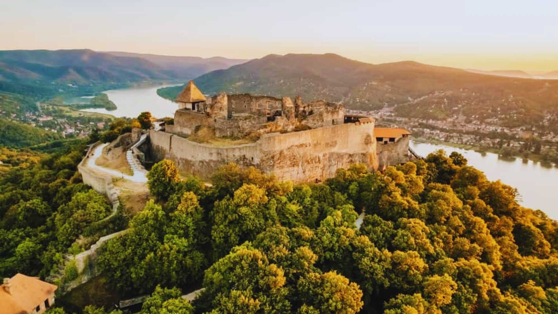 A view of Dracula's castle, situated on the border between Romania and Slovenia, surrounded by lush green hills.